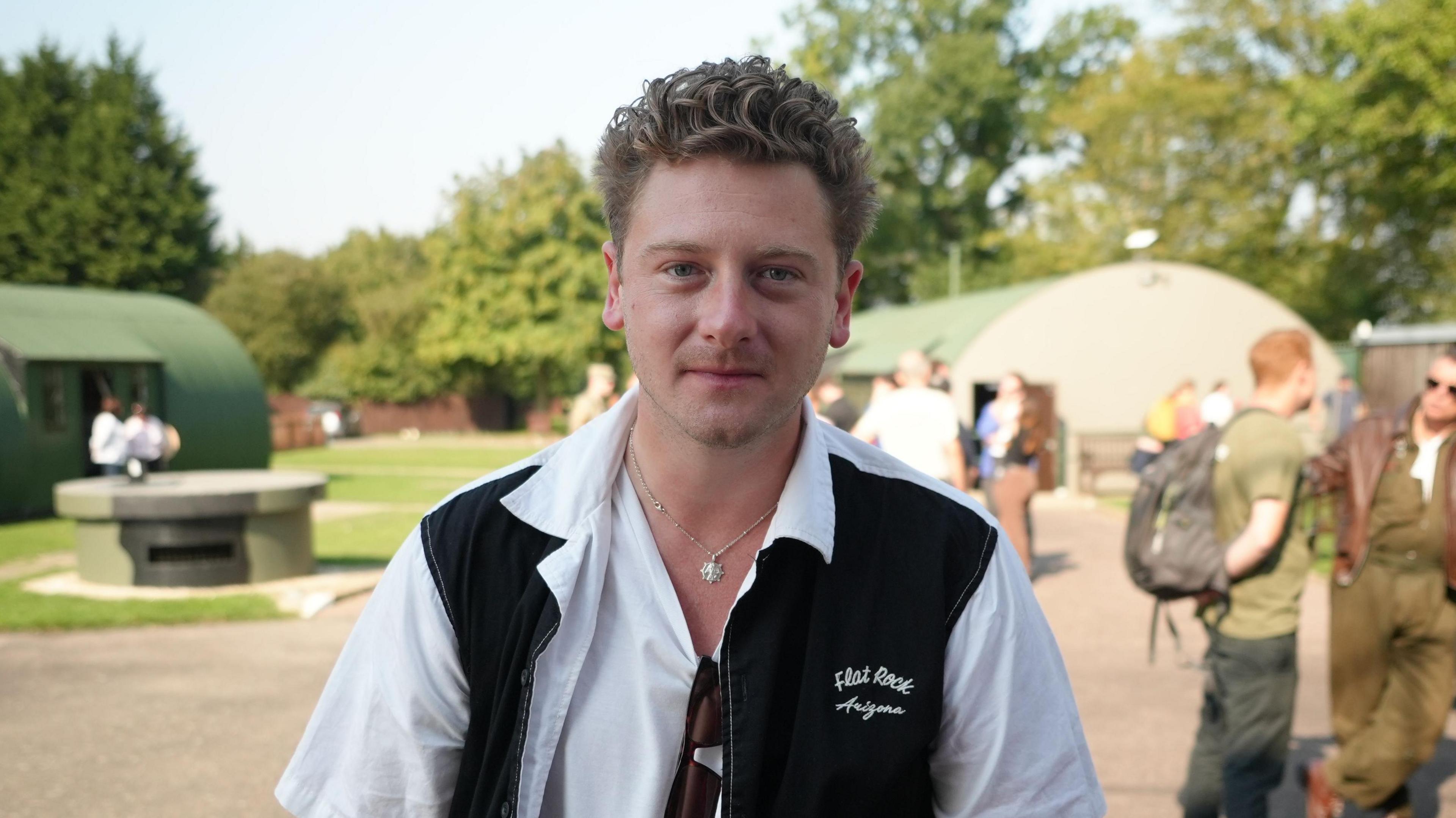 Actor Josh Bolt wearing a black and white shirt and standing in front of military buildings