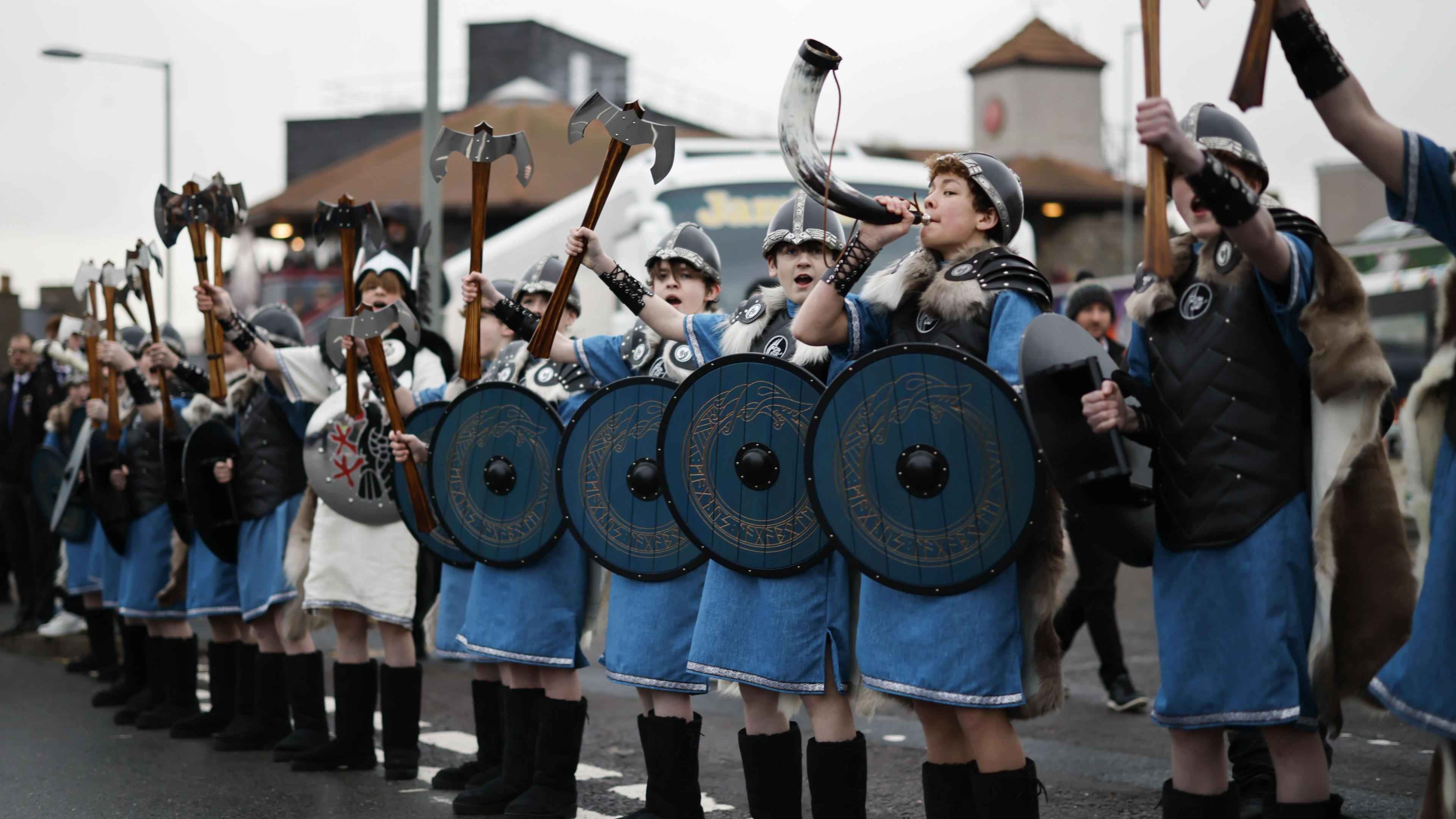 Young members of the Up Helly Aa festival's 'Jarl Squad' blow horns and wave axes during the morning parade in Lerwick, Shetland Islands