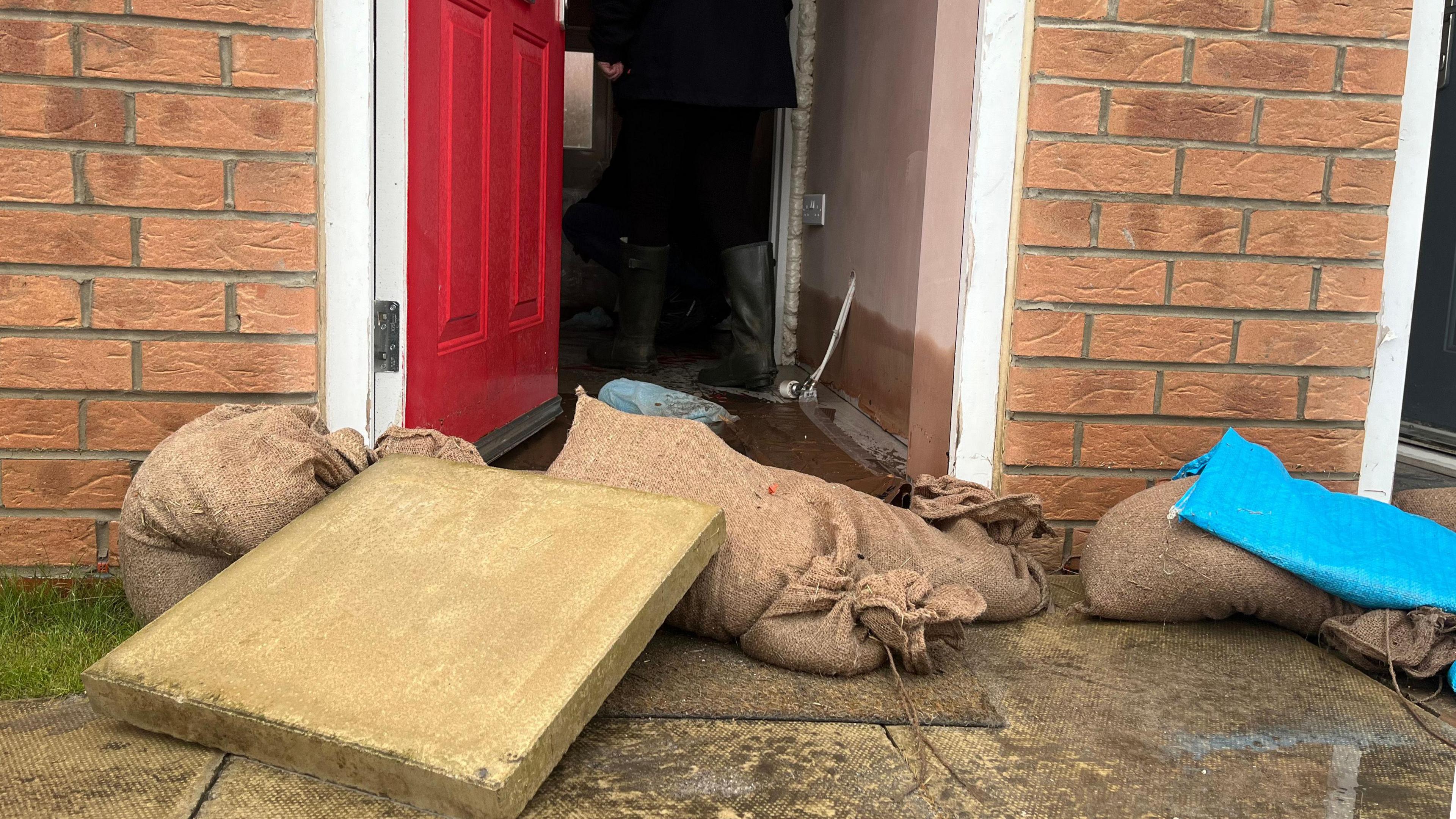 The bottom of a front door has sandbags placed in front of it. The interior of the house has a watermark on the wall that is about a foot high.