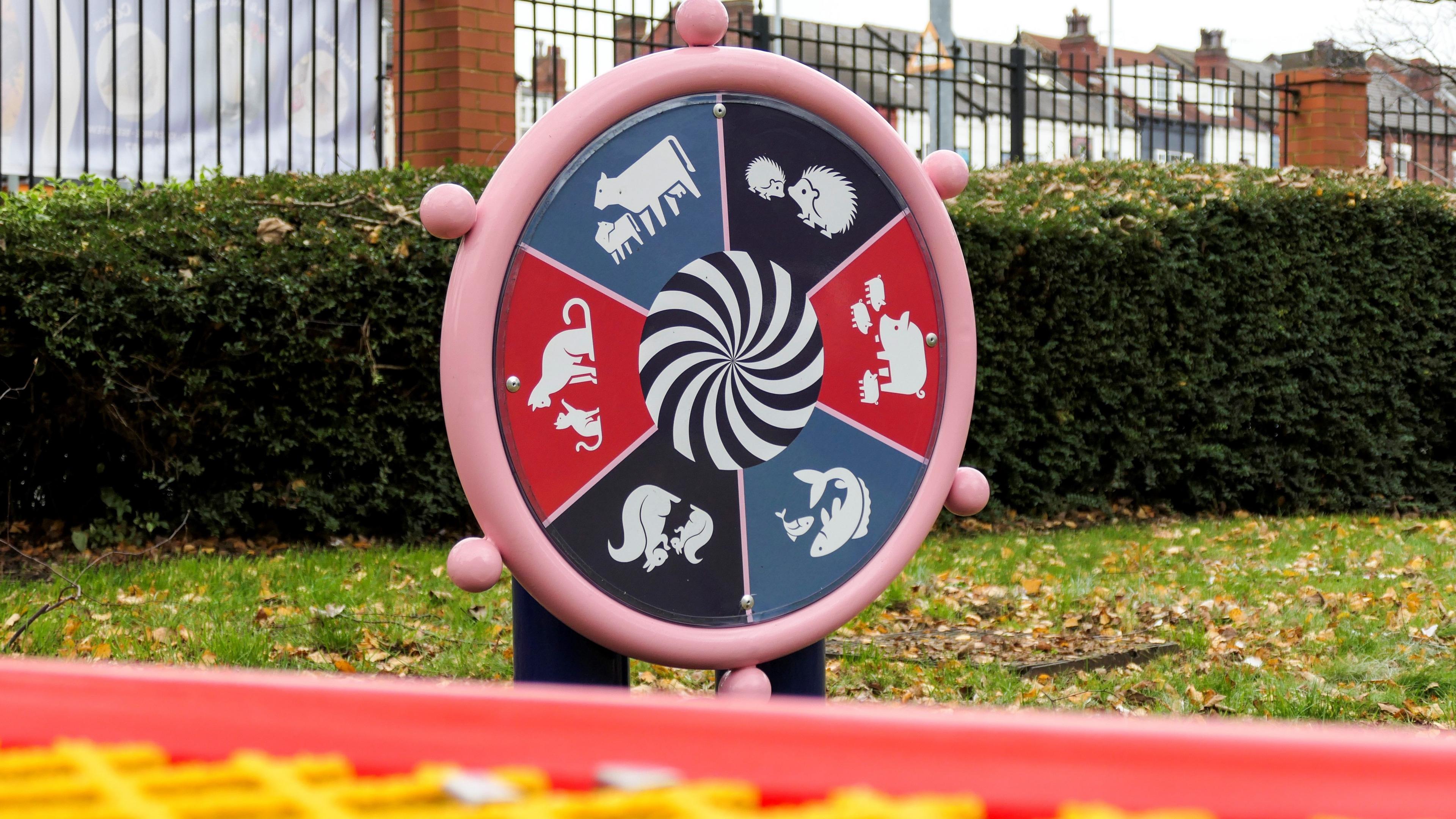 A circular piece of play equipment. It is split into six colourful sections, each one with a different symbol of an animal