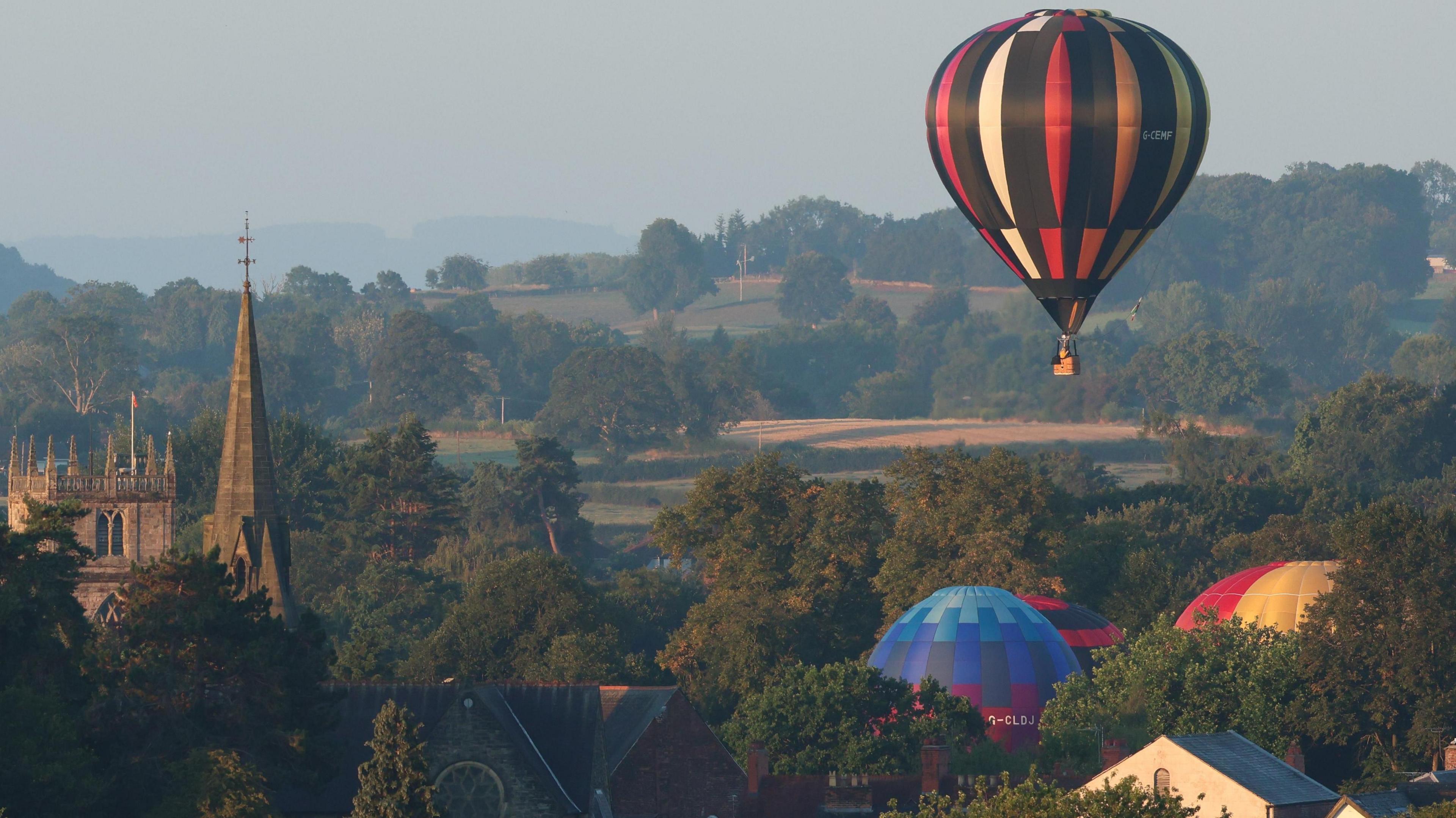 The tops of three giant balloons can be seen peaking over the treetops and buildings in Oswestry with the church of St Oswald also in the background. 