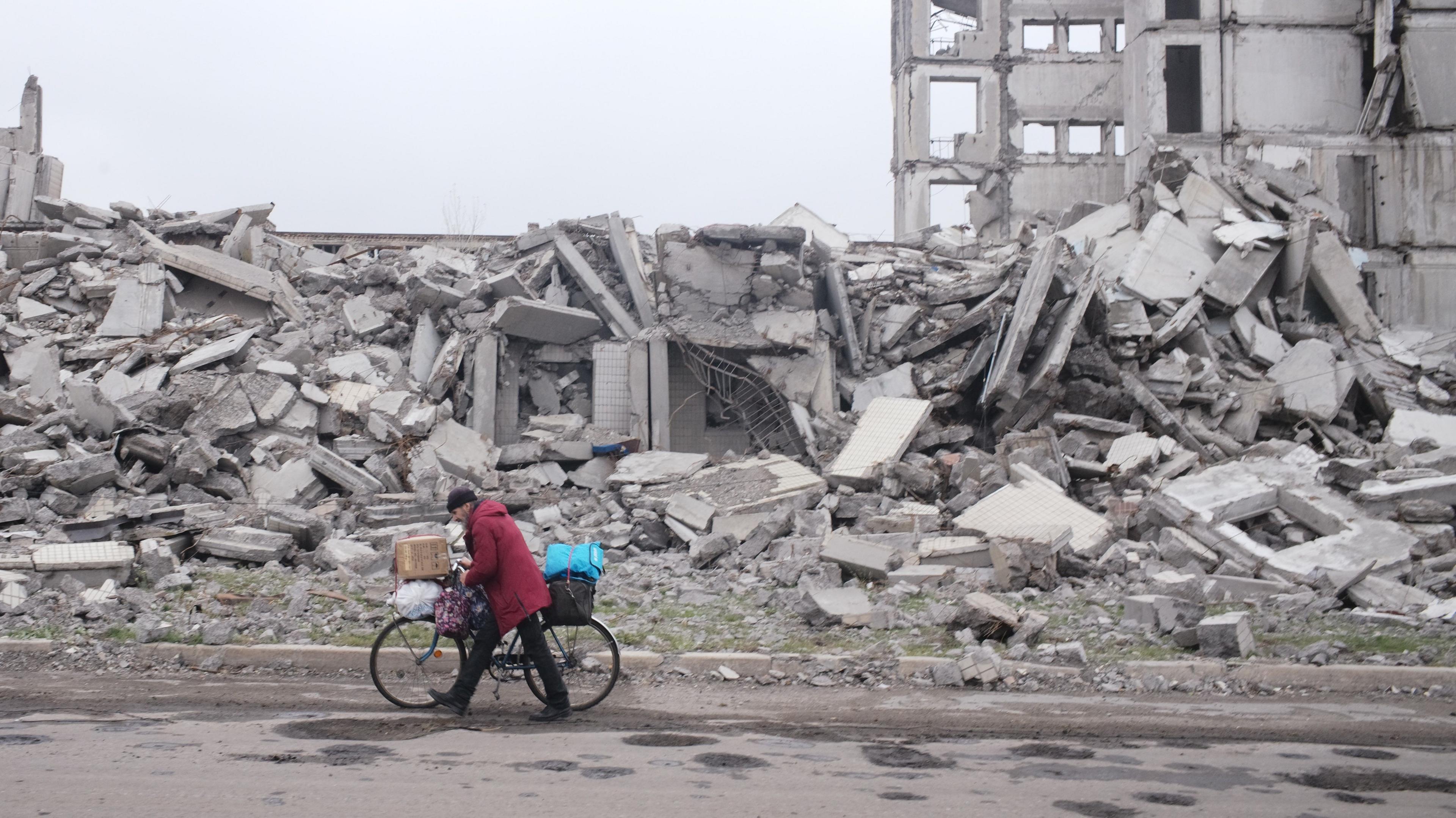 A man walks with a bicycle bearing bags of belongings next to a row of buildings that have been reduced to a pile of rubble in Myrnohrad, Donetsk Oblast, eastern Ukraine