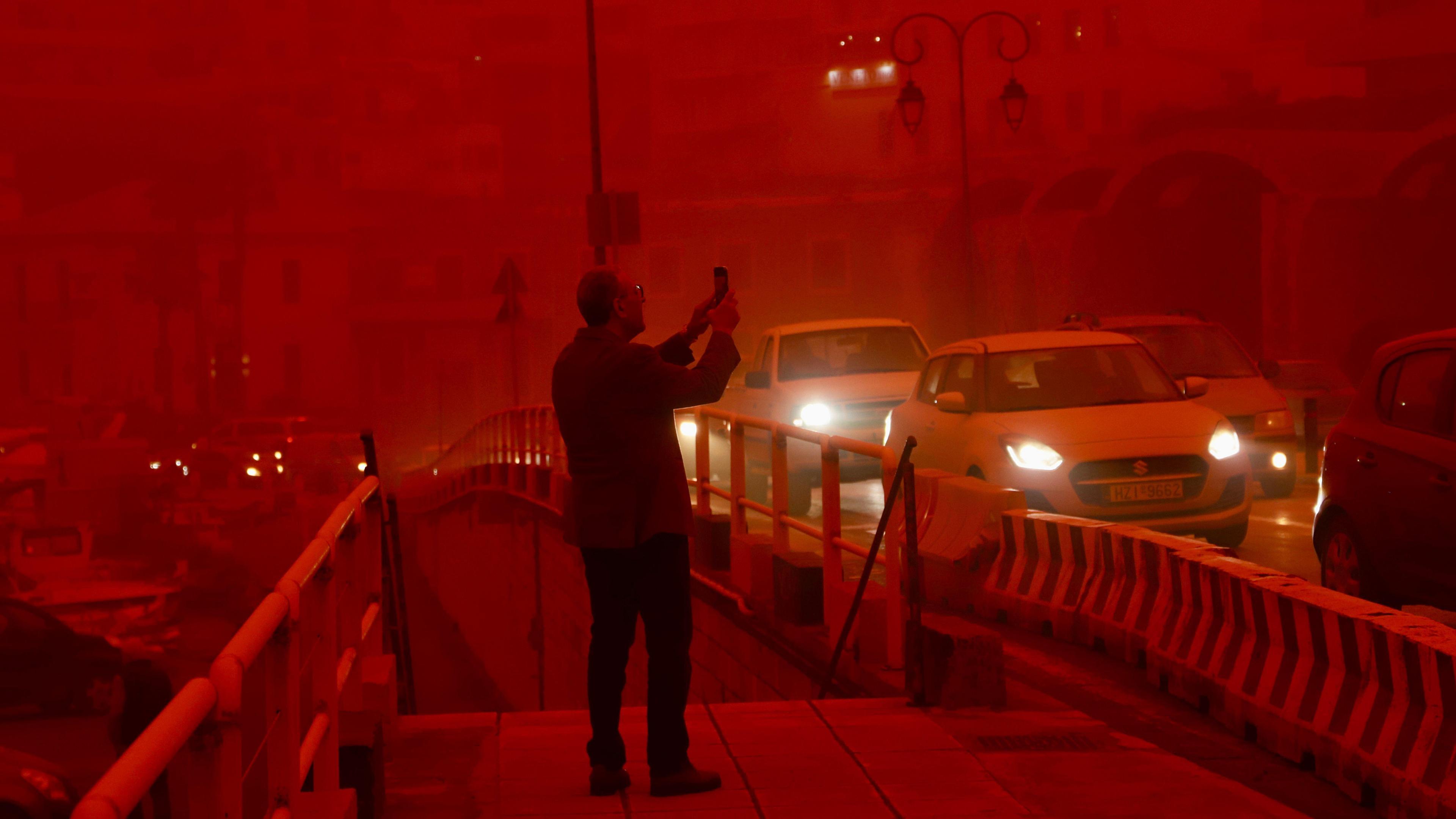 A man takes a picture while cars drive with their headlights on in red air.