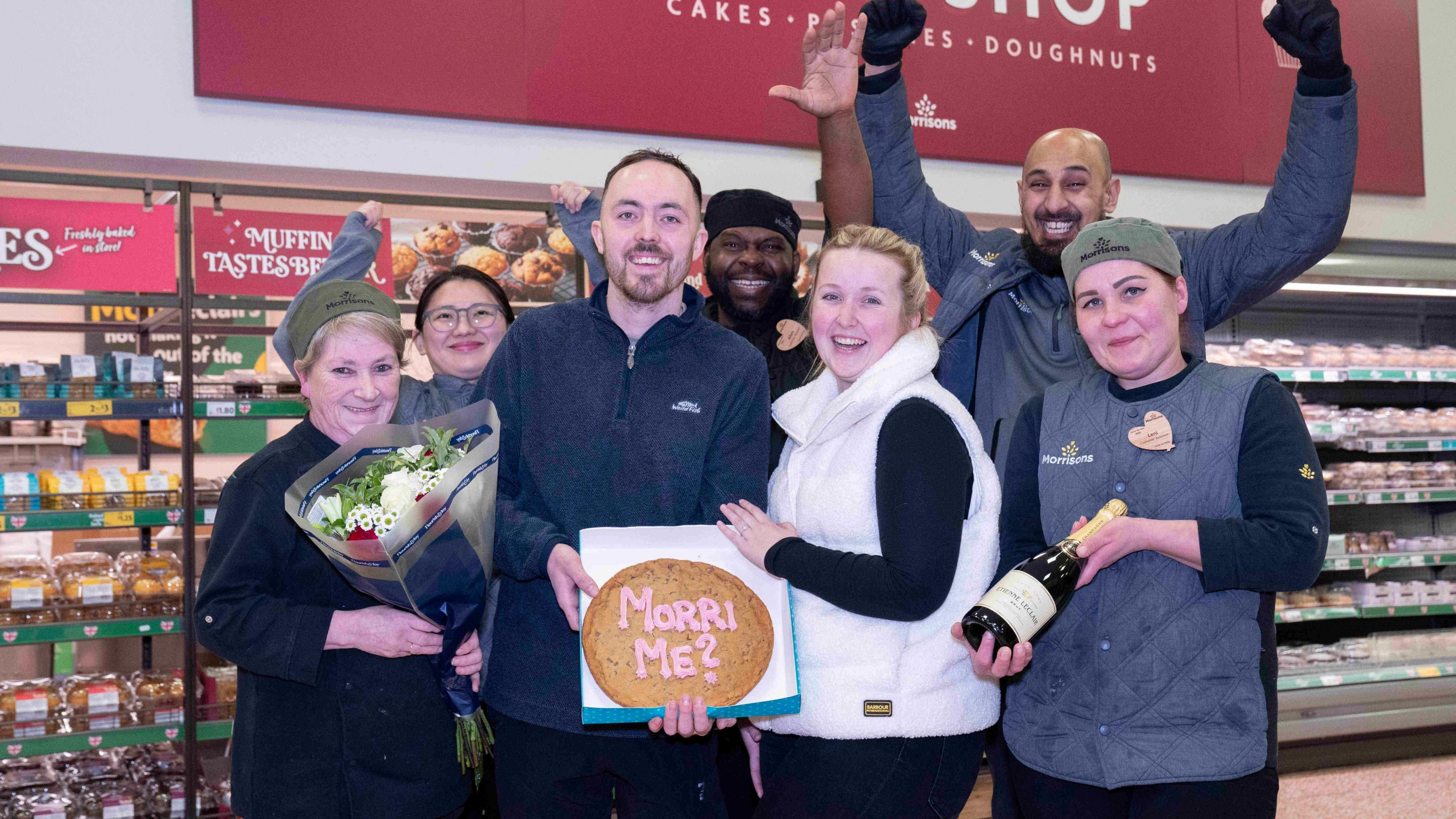 A group of Morrisons employees crowded around Charlie Bullock and Hannah McNaughten at the bakery counter.