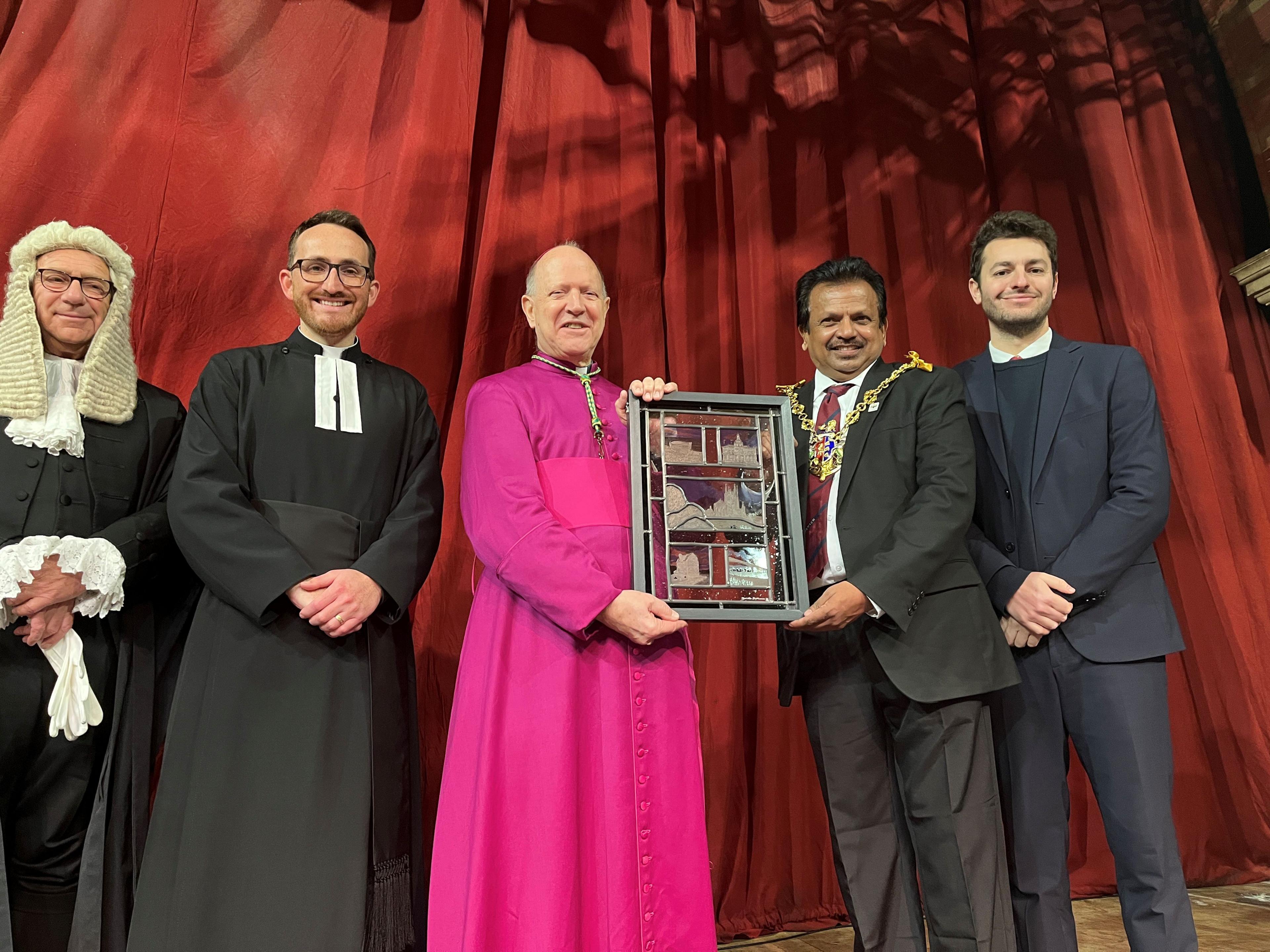 A judge, a vicar, a bishop and mayor and an MP stand in a line. The bishop and mayor are holding a stained glass picture.