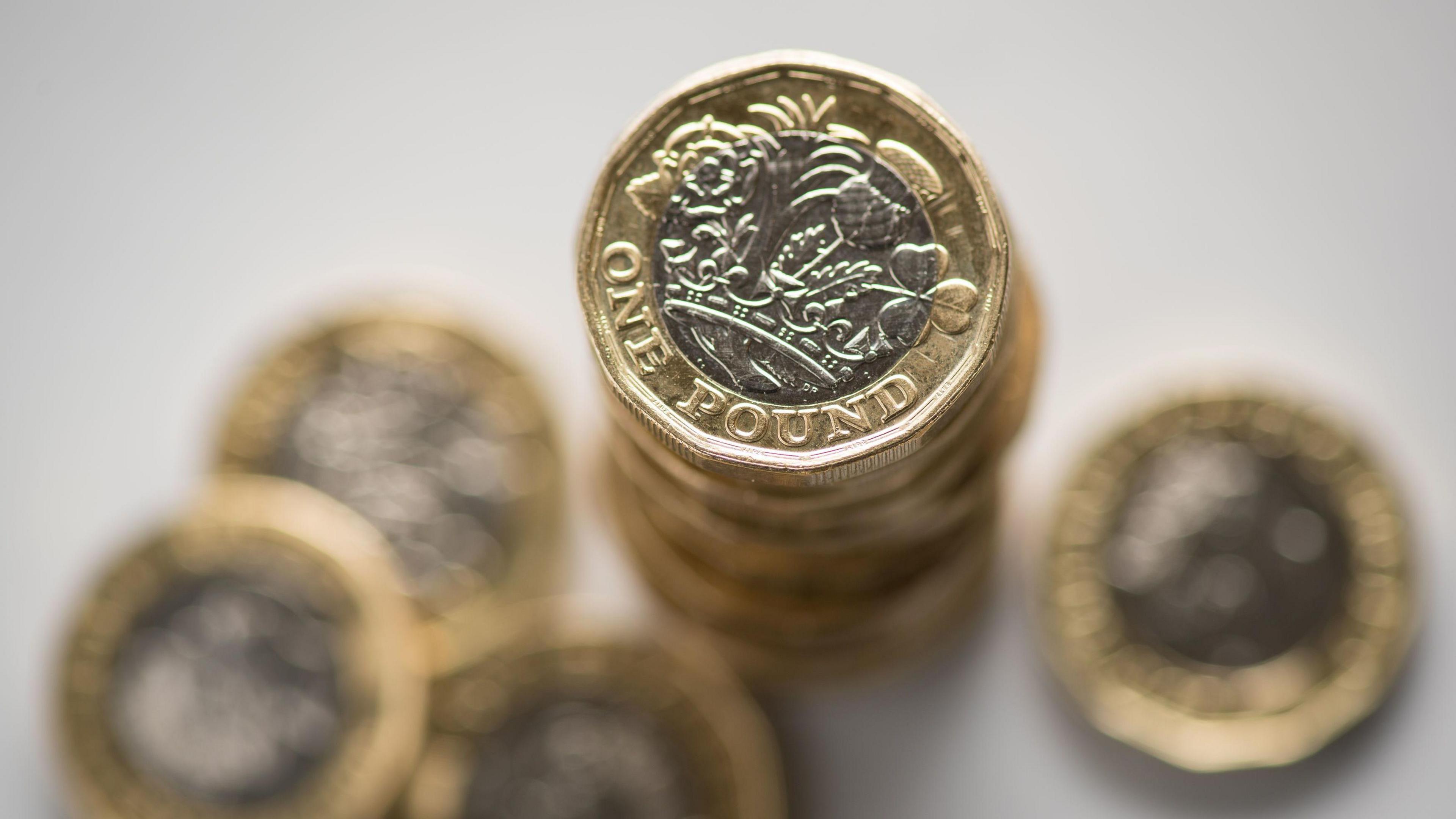 Pound coins stacked up on a white surface