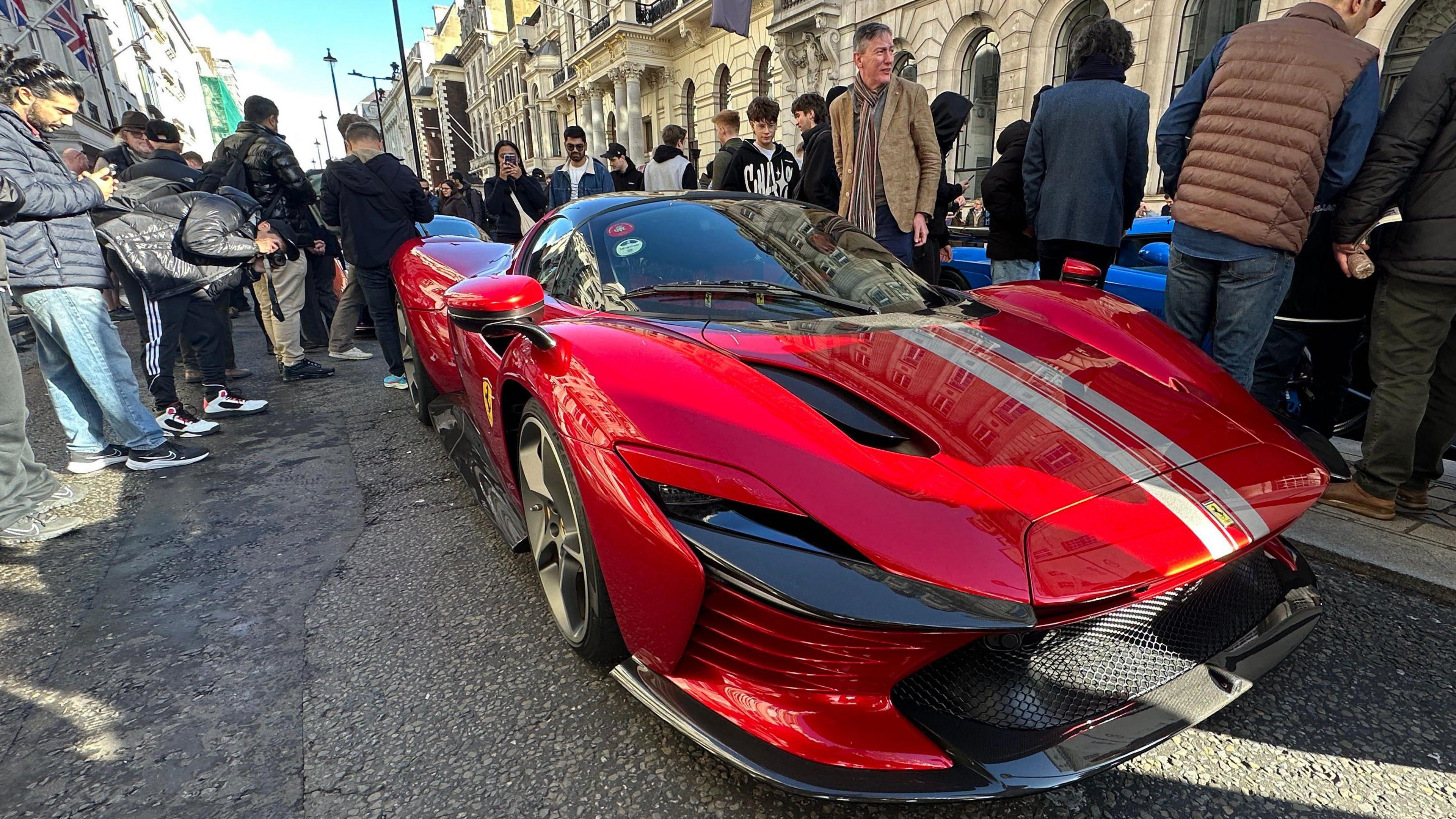A red sports car draws a crowd of young men wearing trainers
