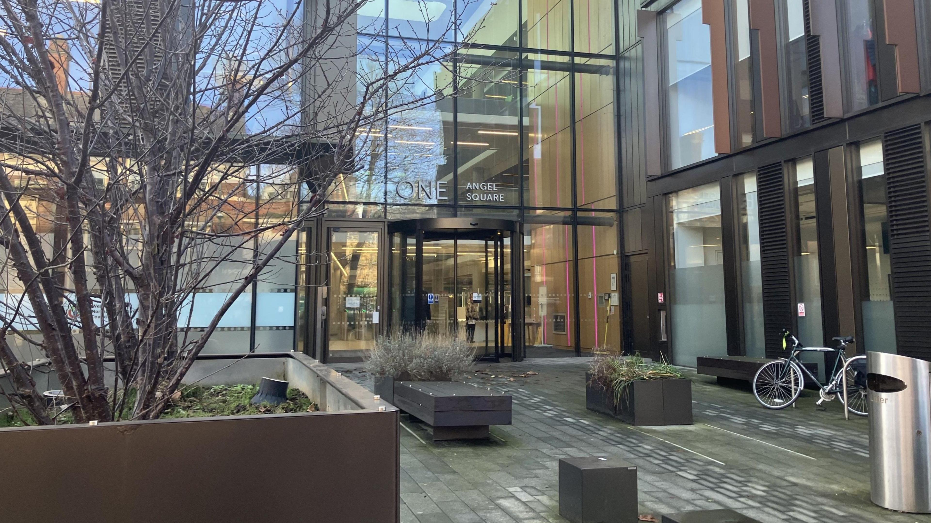 The glass-fronted entrance to West Northamptonshire Council with plants and a bicycle parked outside. 