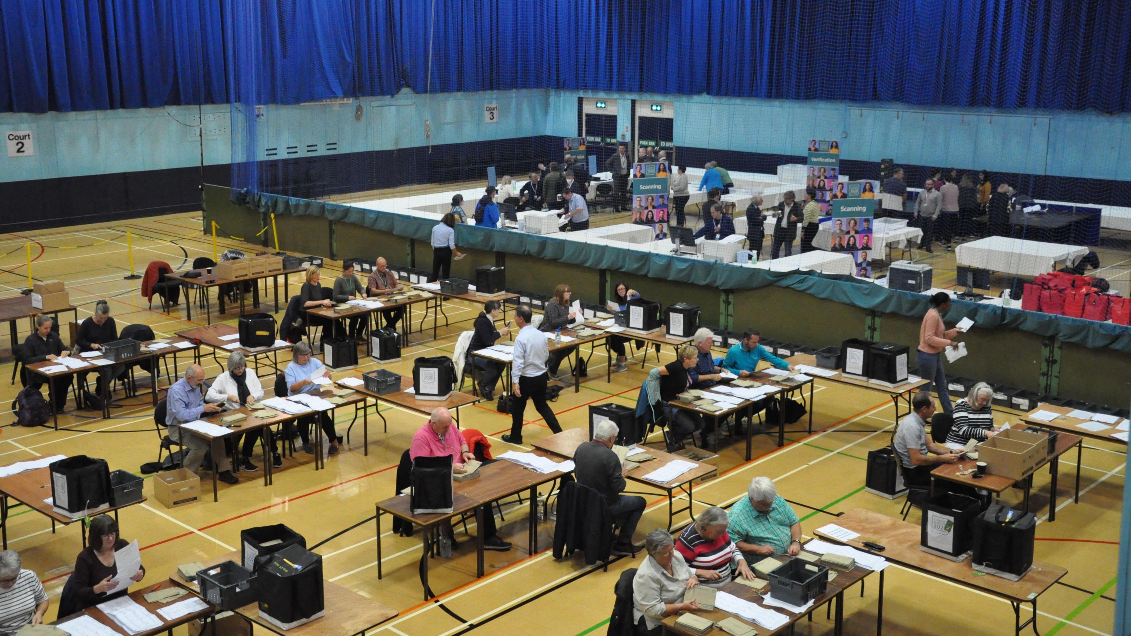 Dozens of people are counting votes in ballot boxes in a gym hall as part of the 2020 Election in Guernsey