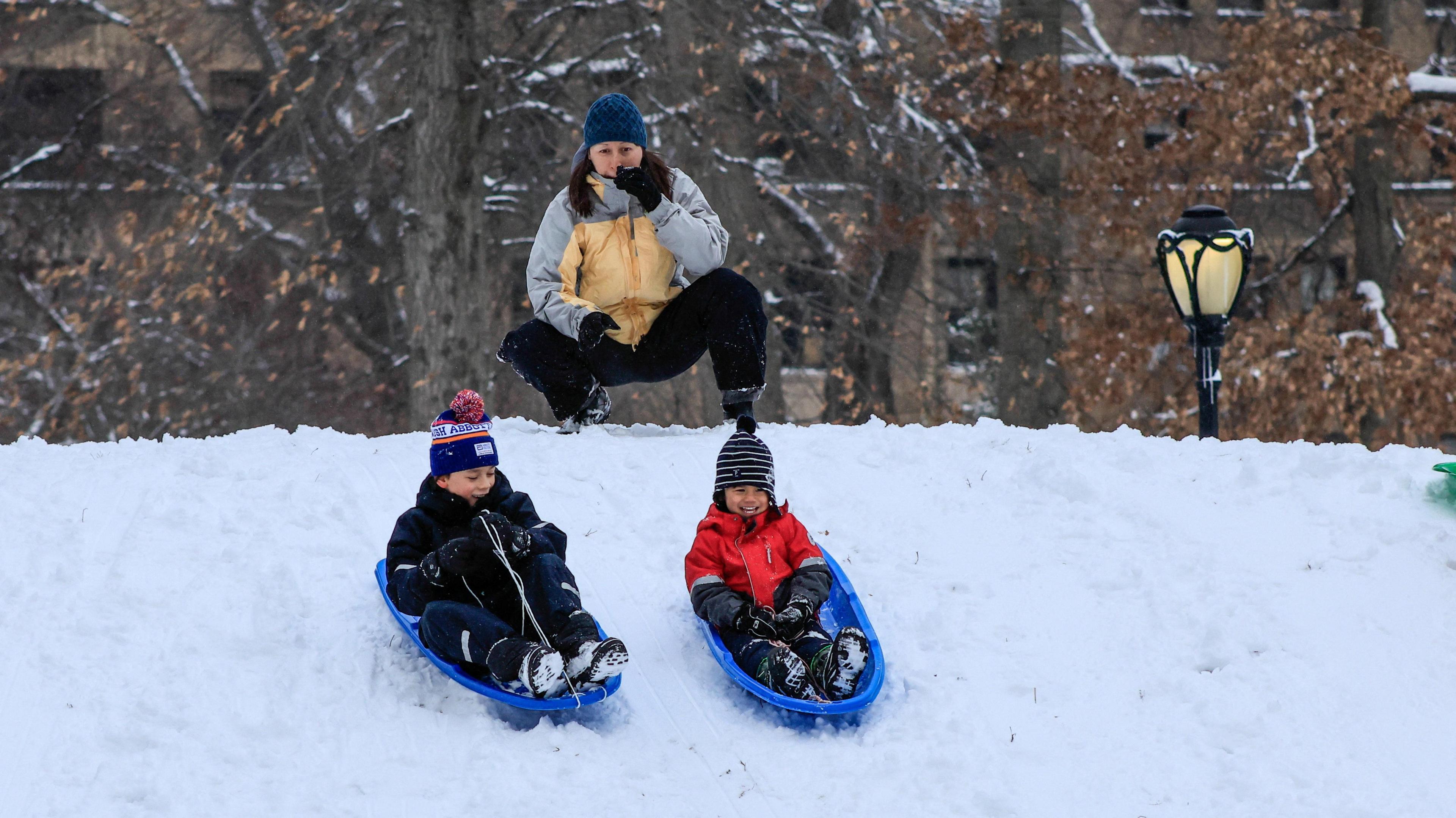 An adult helps two children to sledge in Central Park