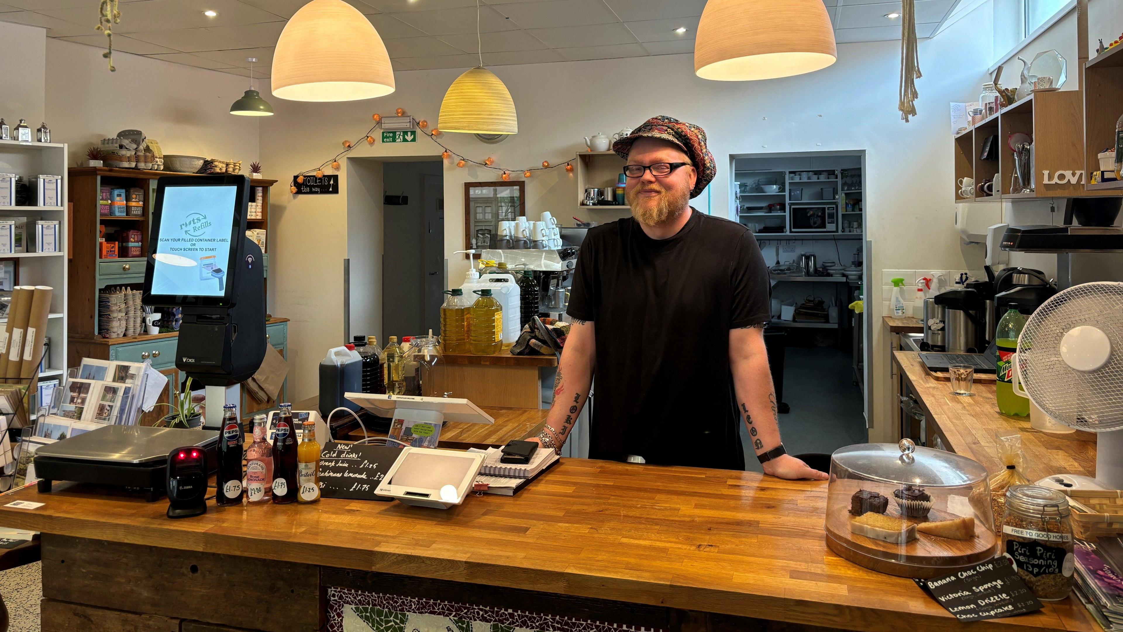 Owen from Roots standing behind the coffee shop counter, smiling