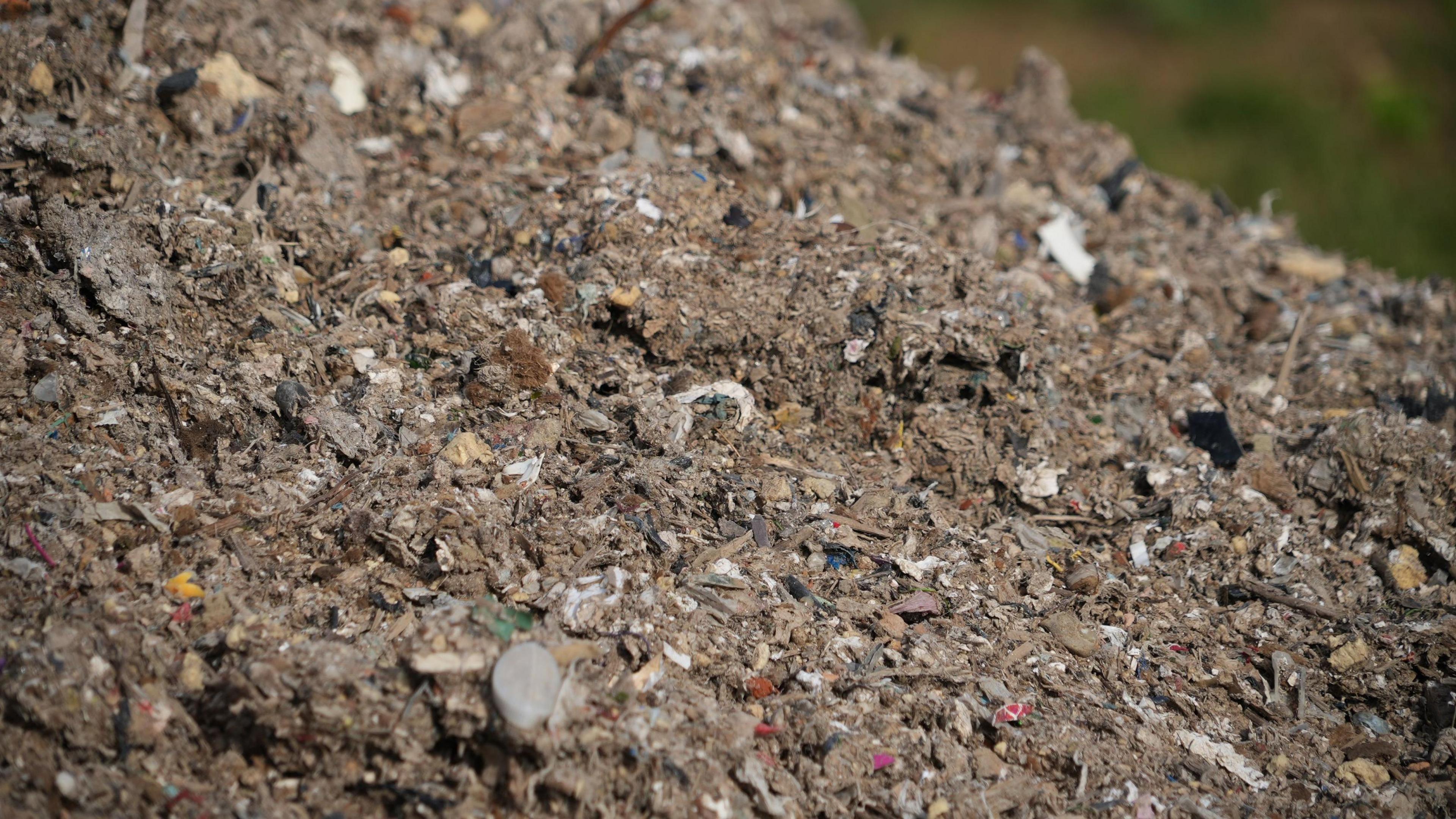 A huge pile of brown waste with white flecks of plastic dotted in the mass. 