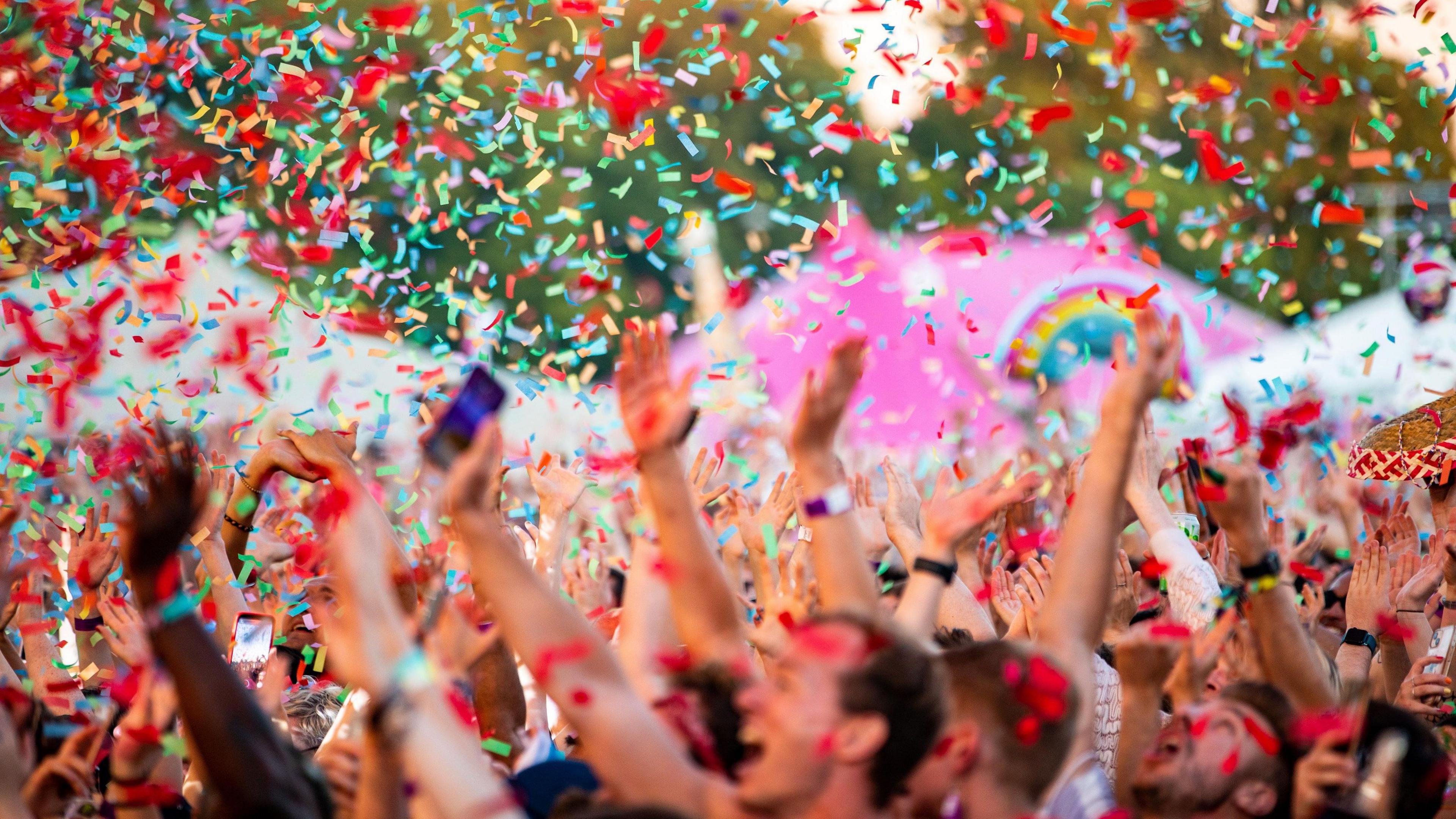 A picture of the crowd cheering as rainbow confetti falls. 