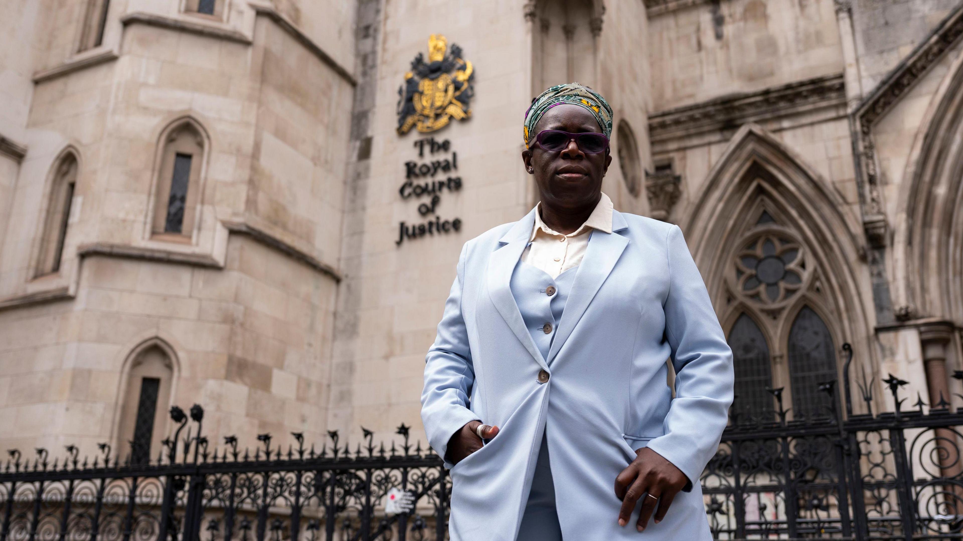 Rosamund Adoo-Kissi-Debrah, wearing a light blue suit, stands outside the High Court in central London