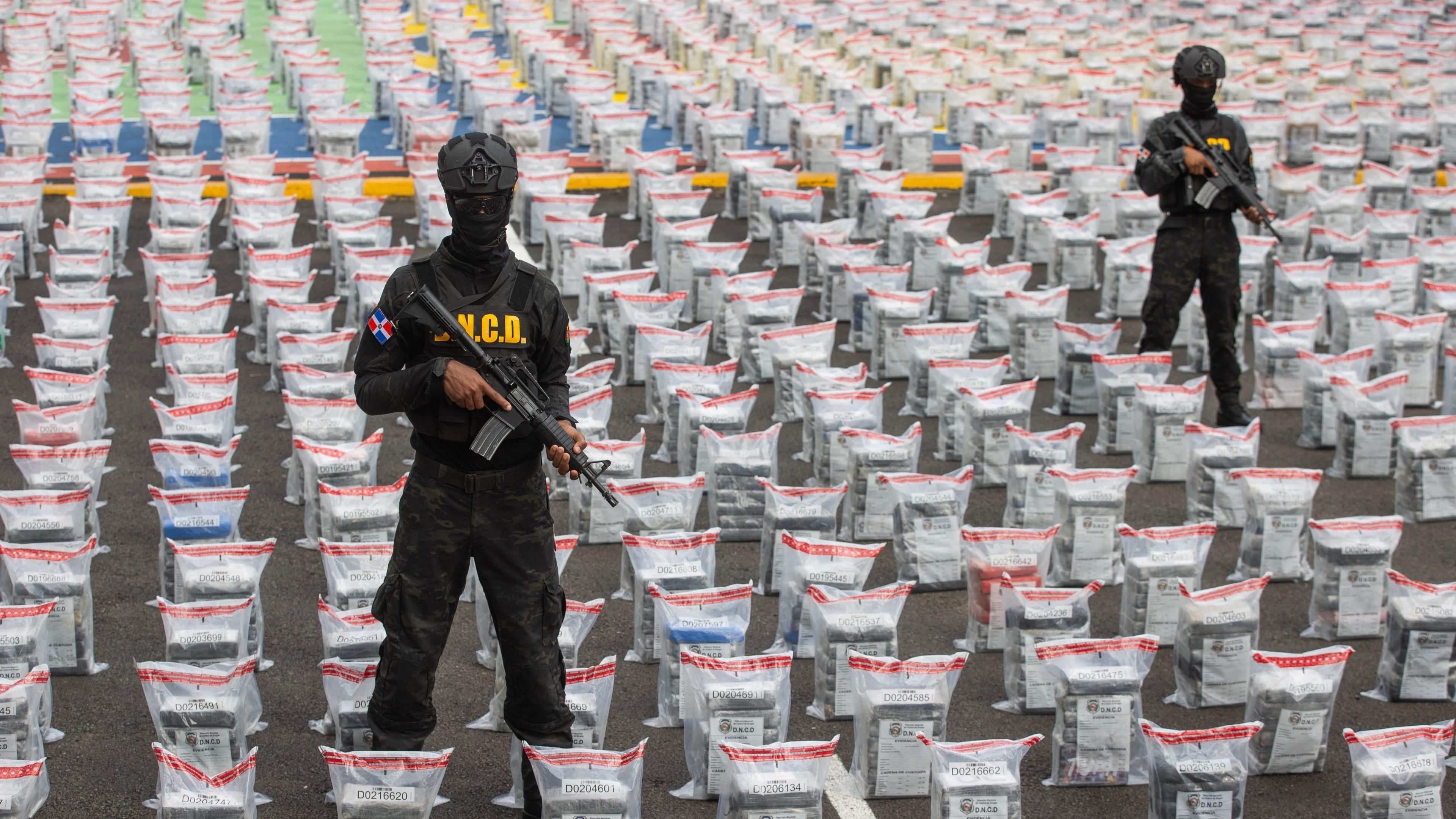 Police officers standing with guns in front of bags of cocaine