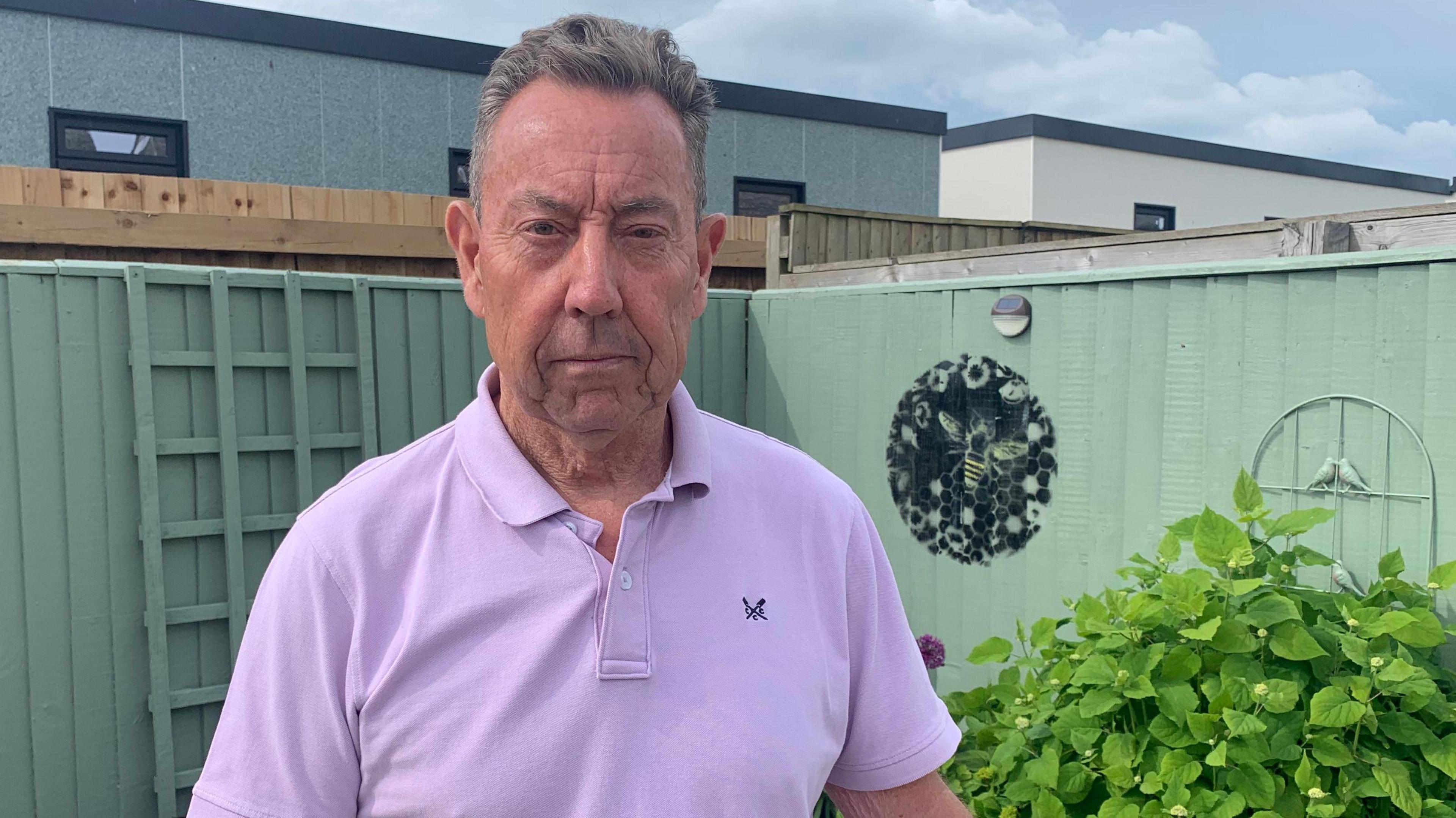 A picture of Steve McGranaghan in his garden with new buildings behind him