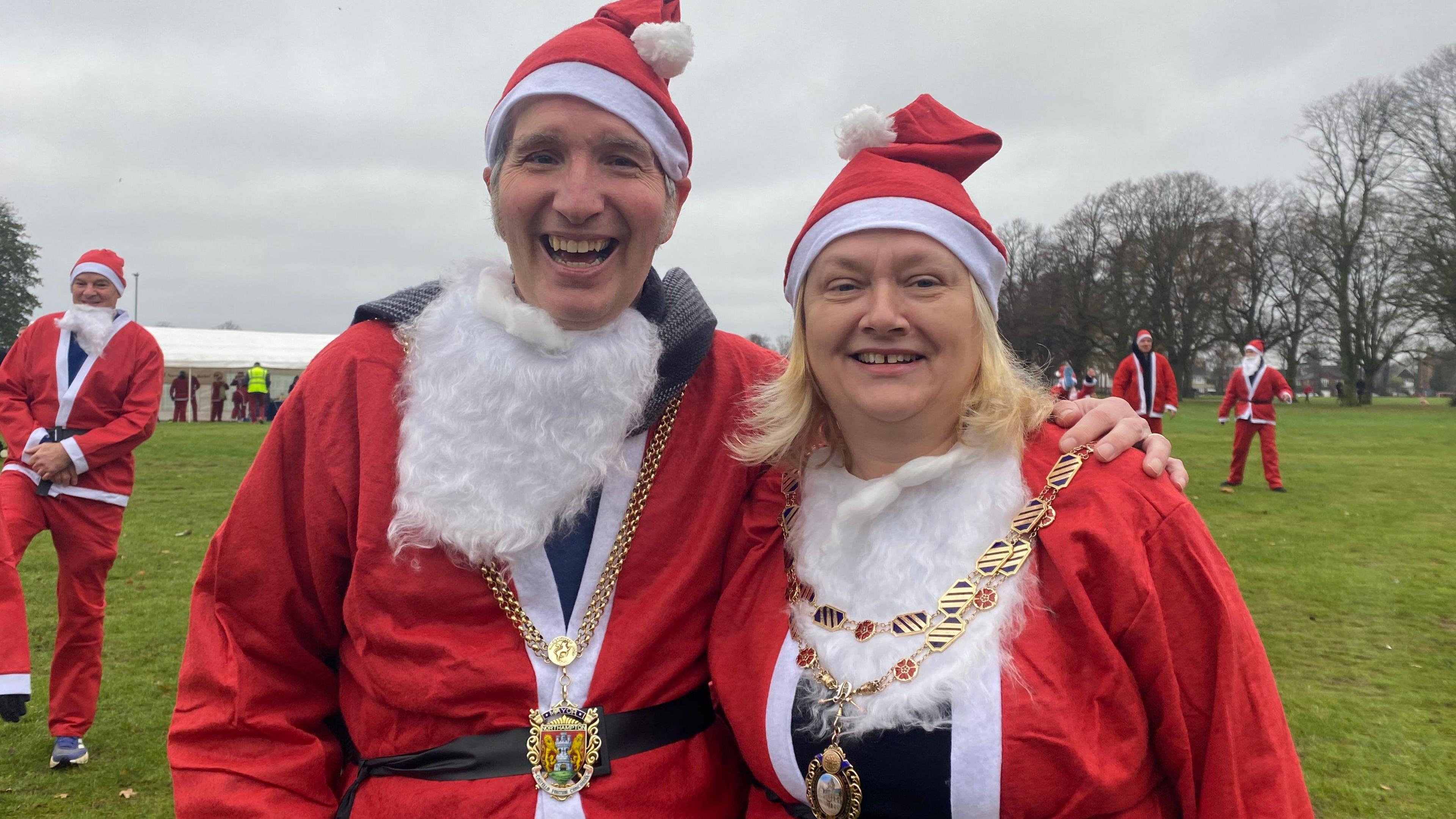 Mayor and Mayoress, Paul and Mylissa Joyce staring at the camera smiling. They are wearing gold chains. They both have red santa hats on and red and white jackets. 