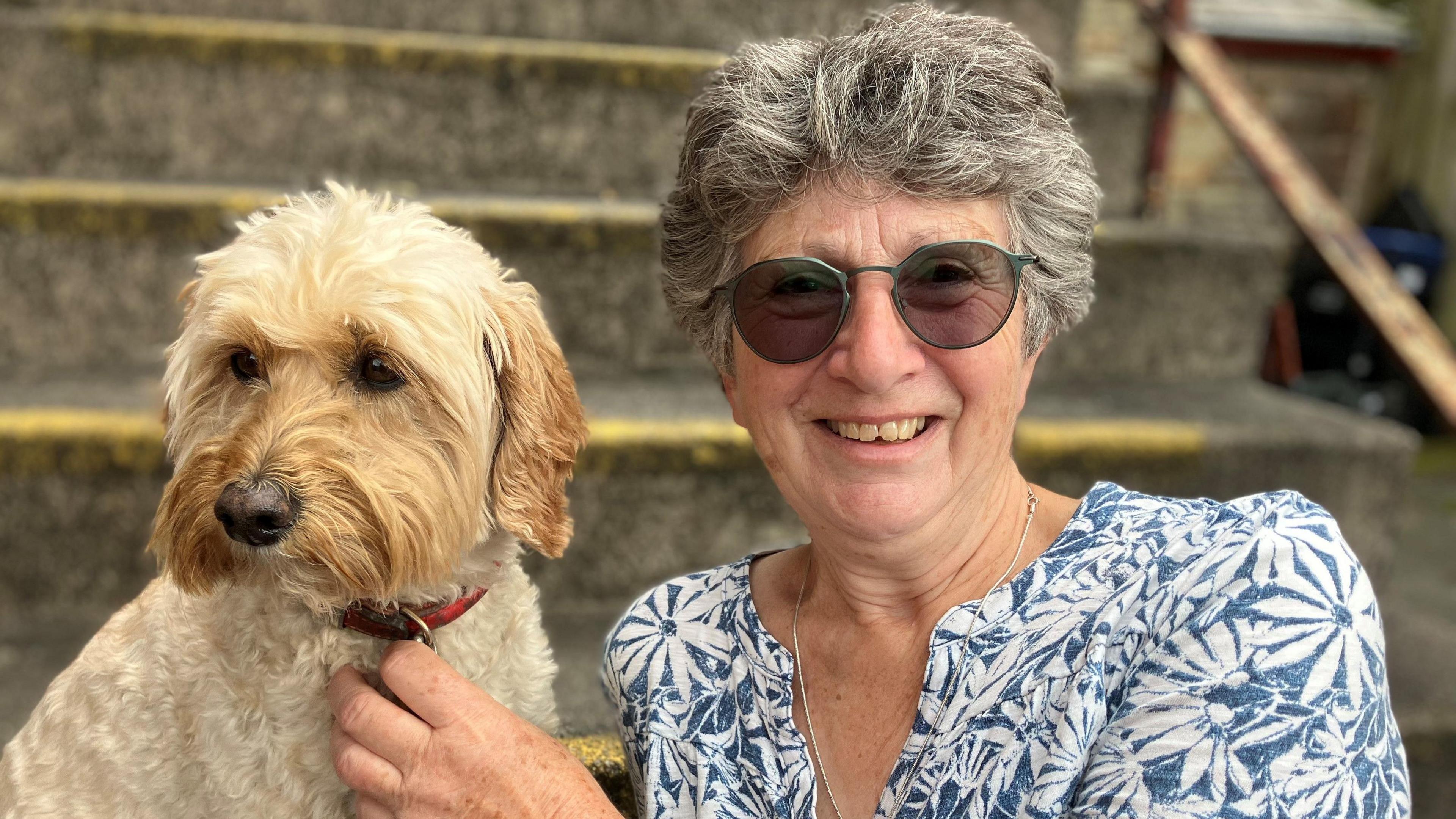 Woman wearing glasses with grey hair holding the collar of a dog