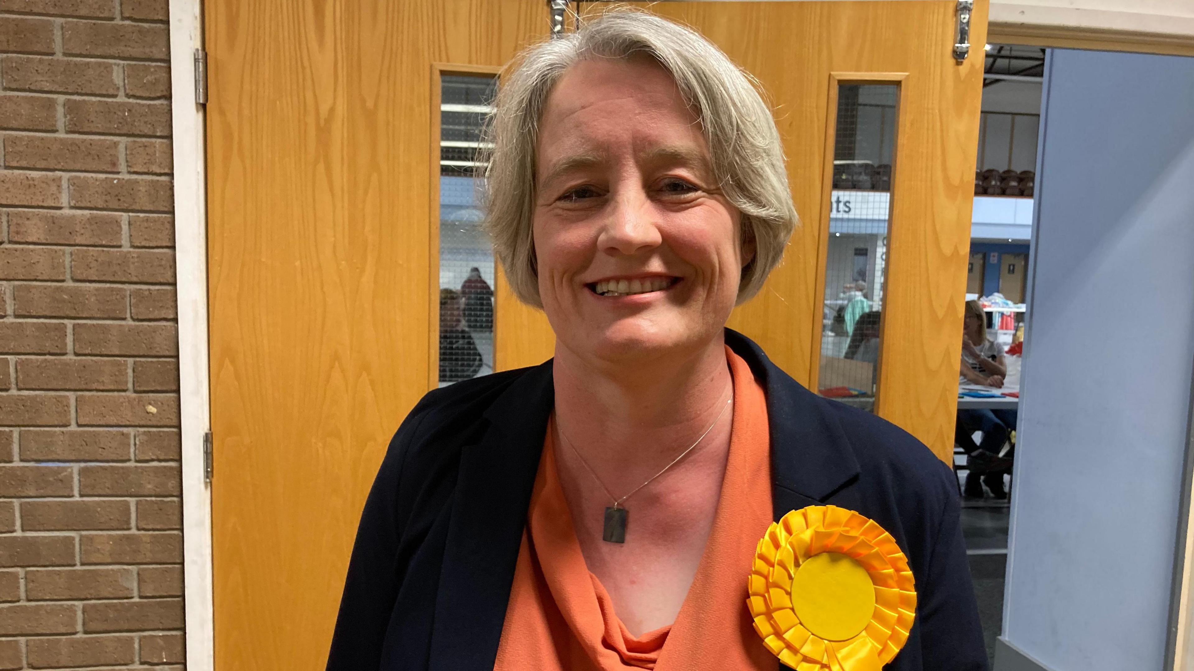 Claire Young wearing a yellow rosette smiling at the camera