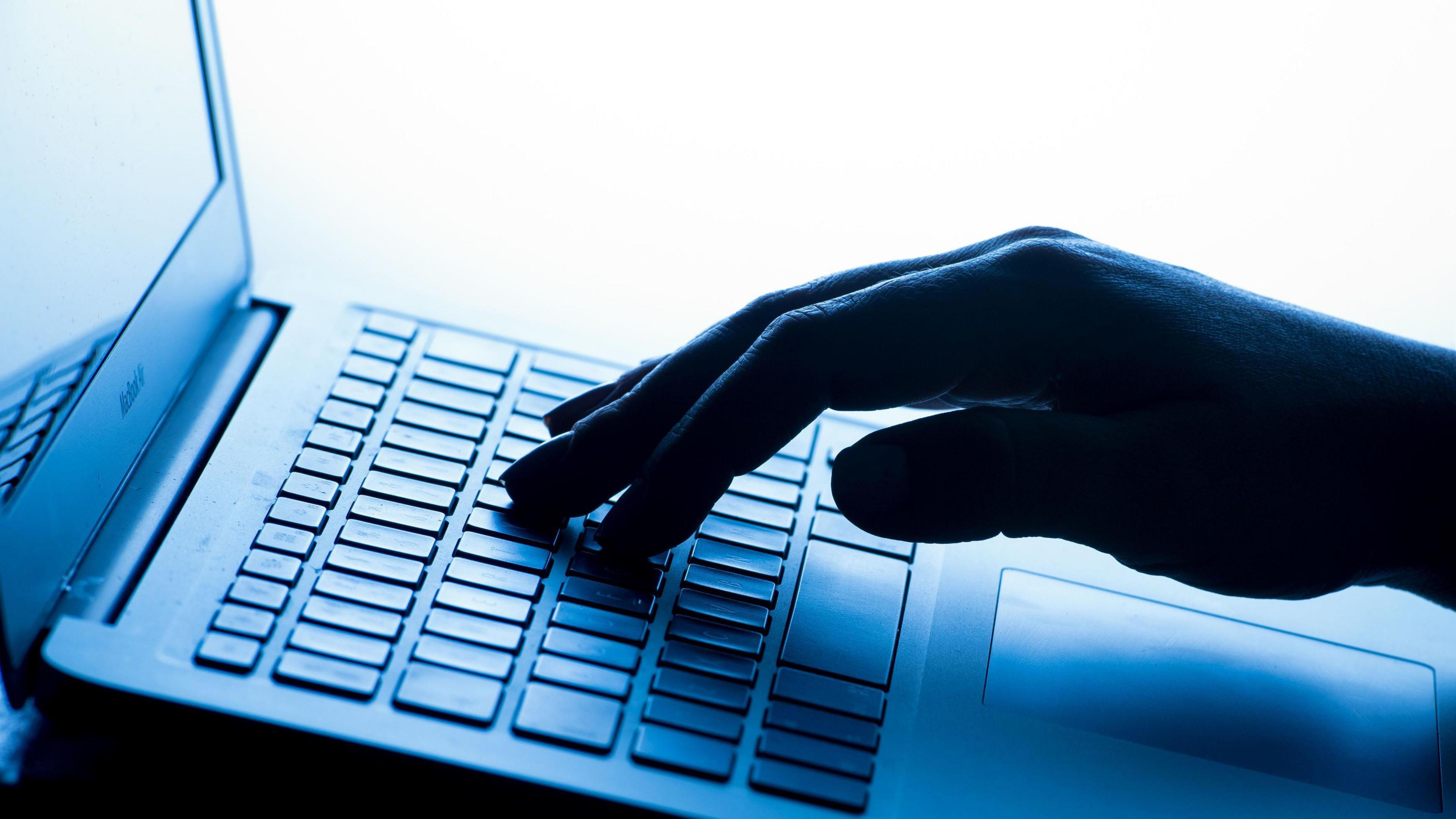 A laptop against a bright background with one hand resting on the keyboard