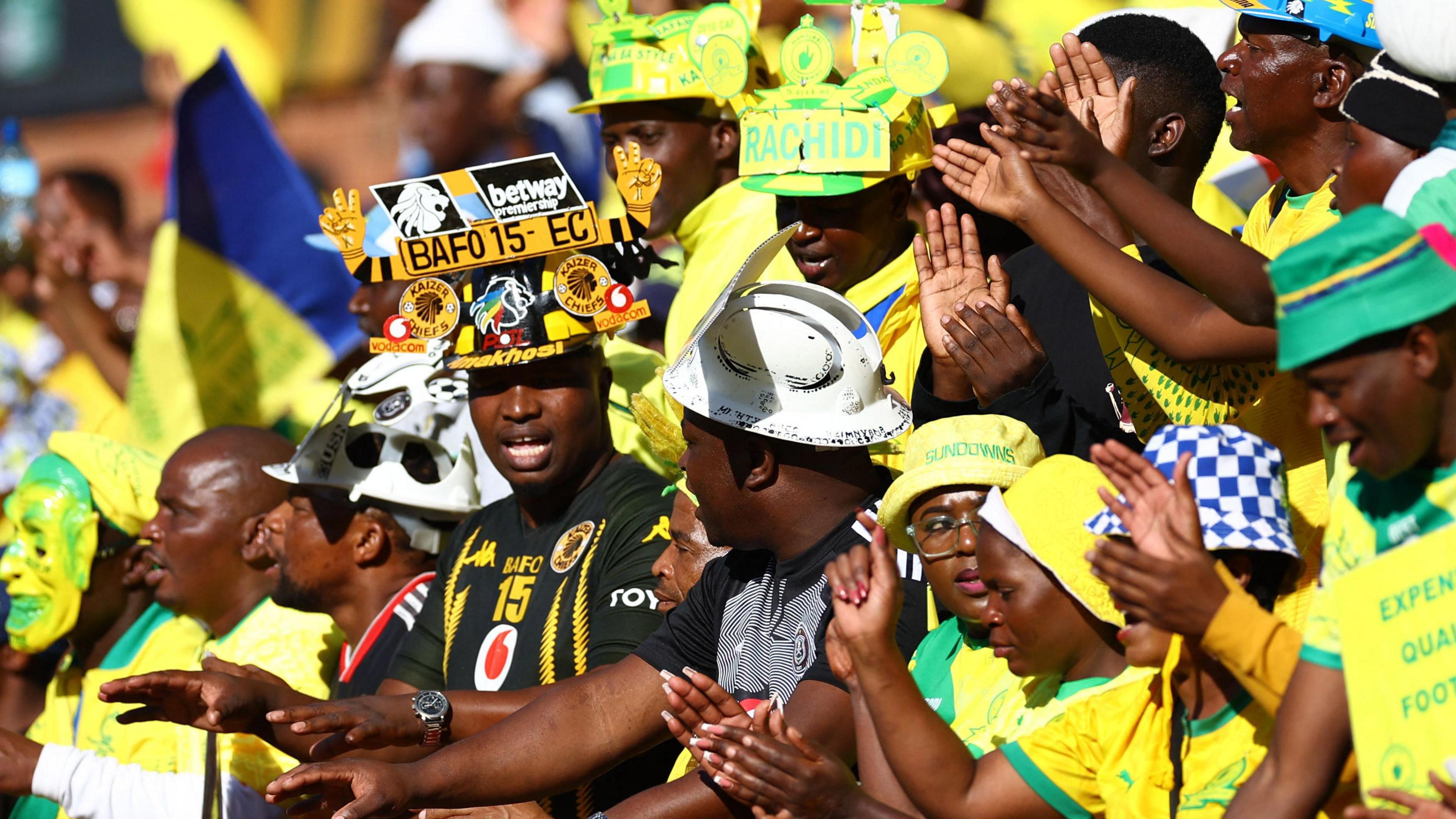 Mamelodi Sundowns fans dance in a stand wearing the club's yellow and green colours and a selection of colourful and unusual hats