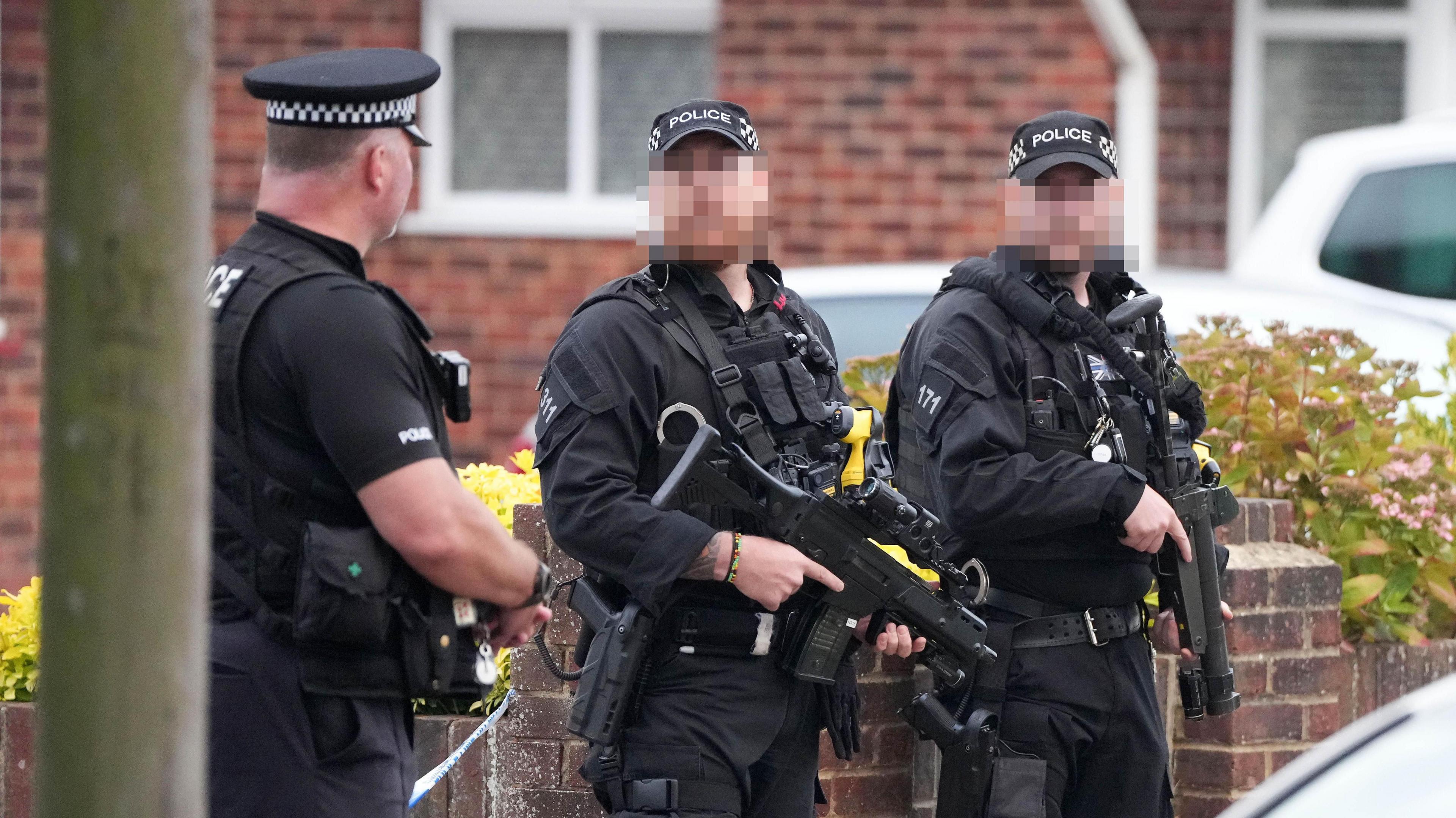 Three armed police at the scene of an incident in Lindum Road, Worthing. Two of the officers' faces are blurred out. All three are wearing black uniform and police caps. Two guns are visible in the image.