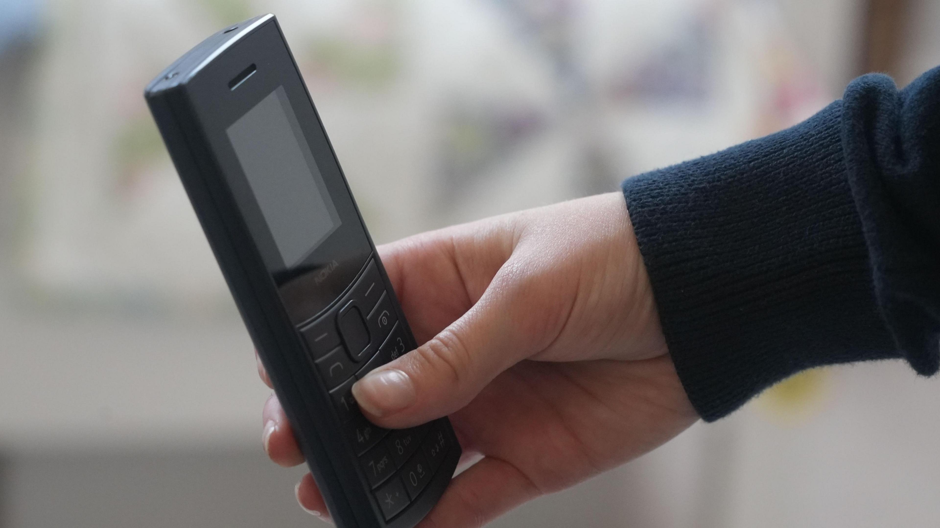 A child holds and old black mobile phone