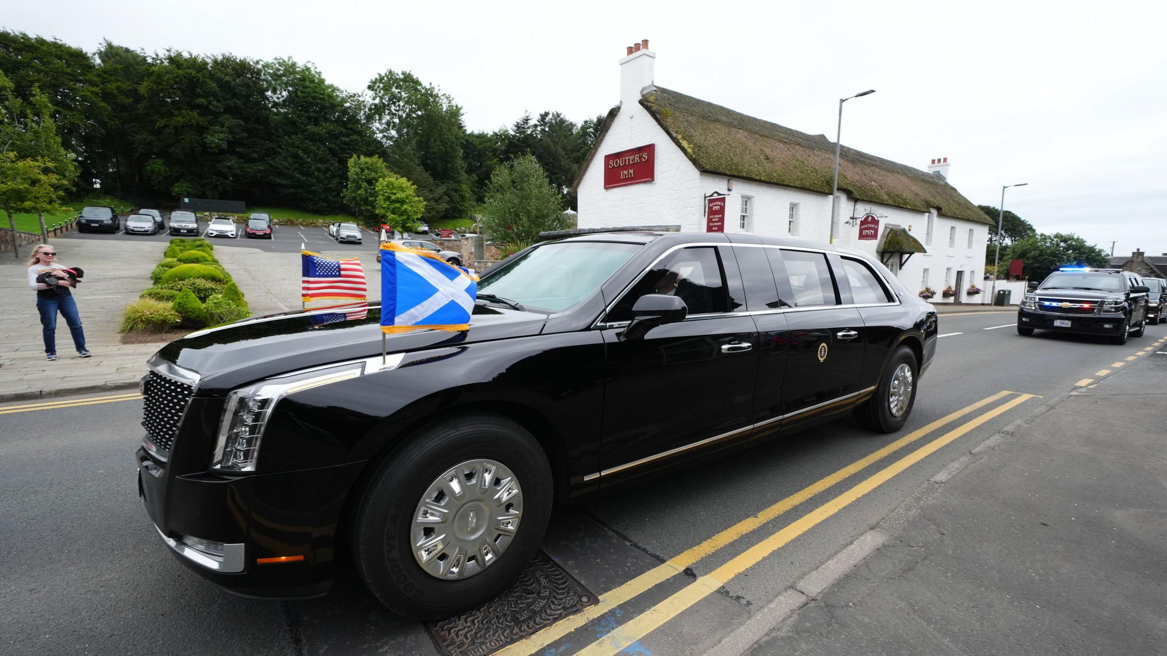 The presidential car with the flags of the US and Scotland flying from the bonnet passed through a Scottish village - a low building with a thatched roof is in the background.