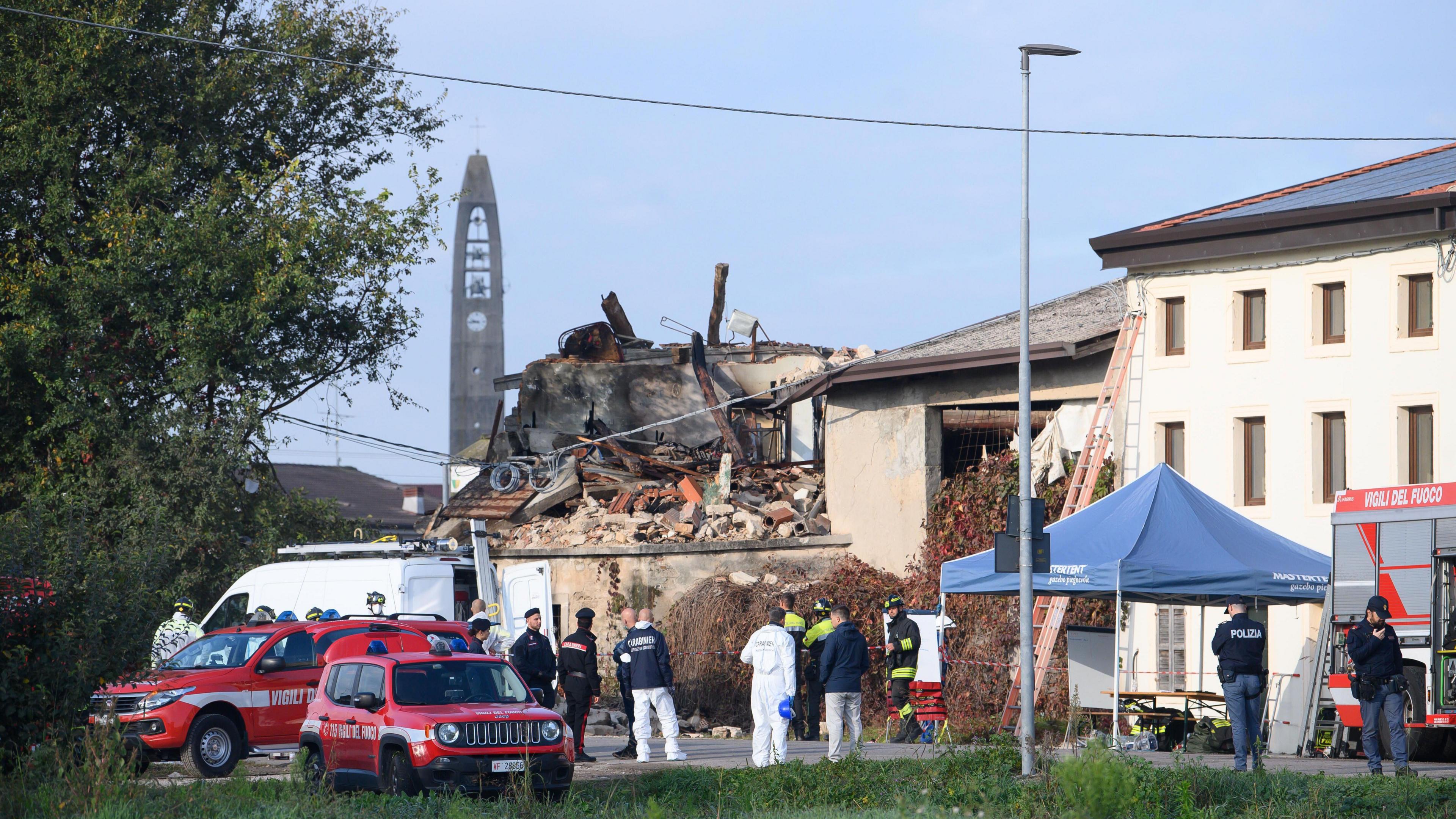 A building reduced to rubble with emergency services cars parked in front of it