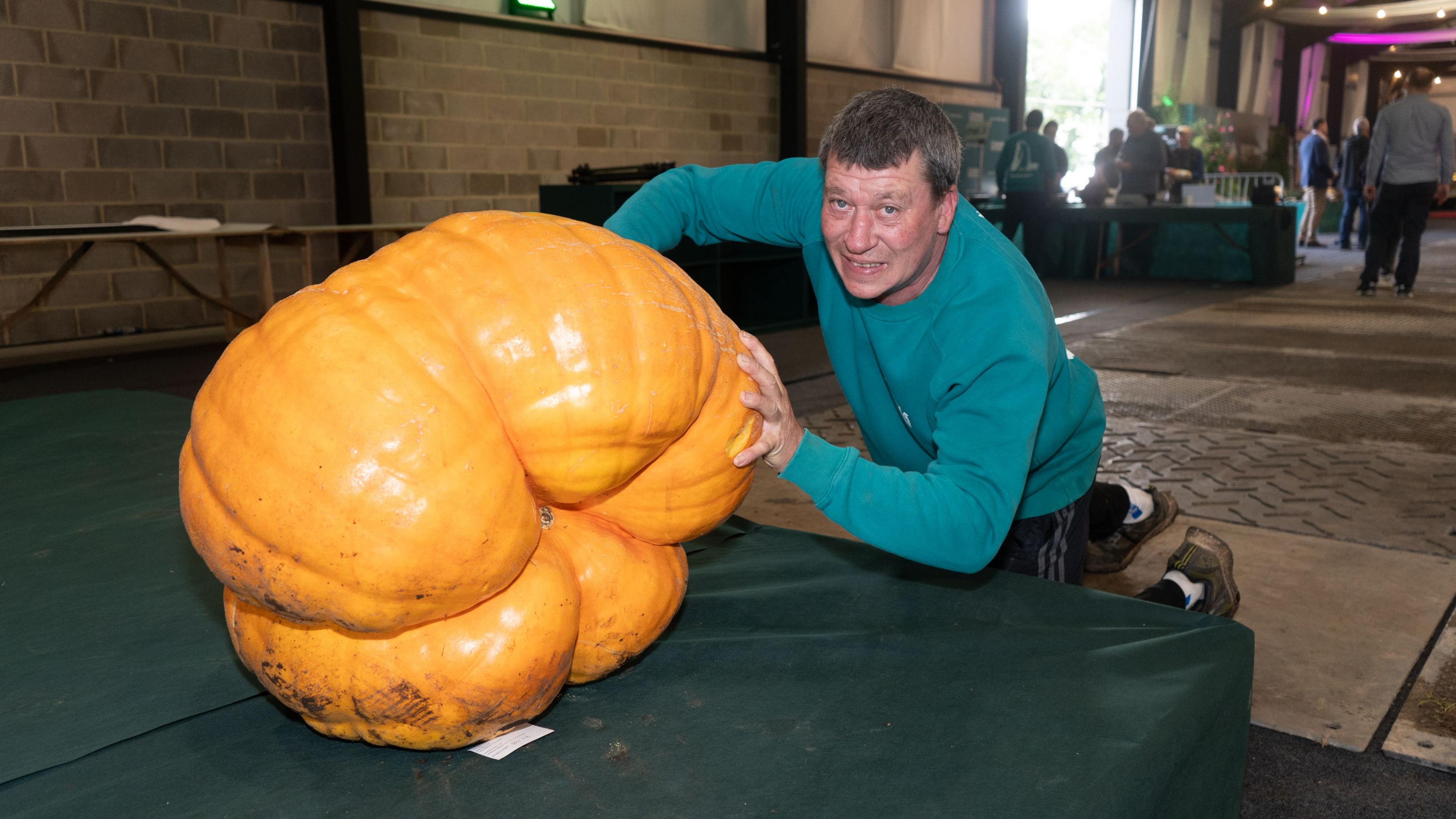 A man grimacing and his pretends to push a large pumpkin.