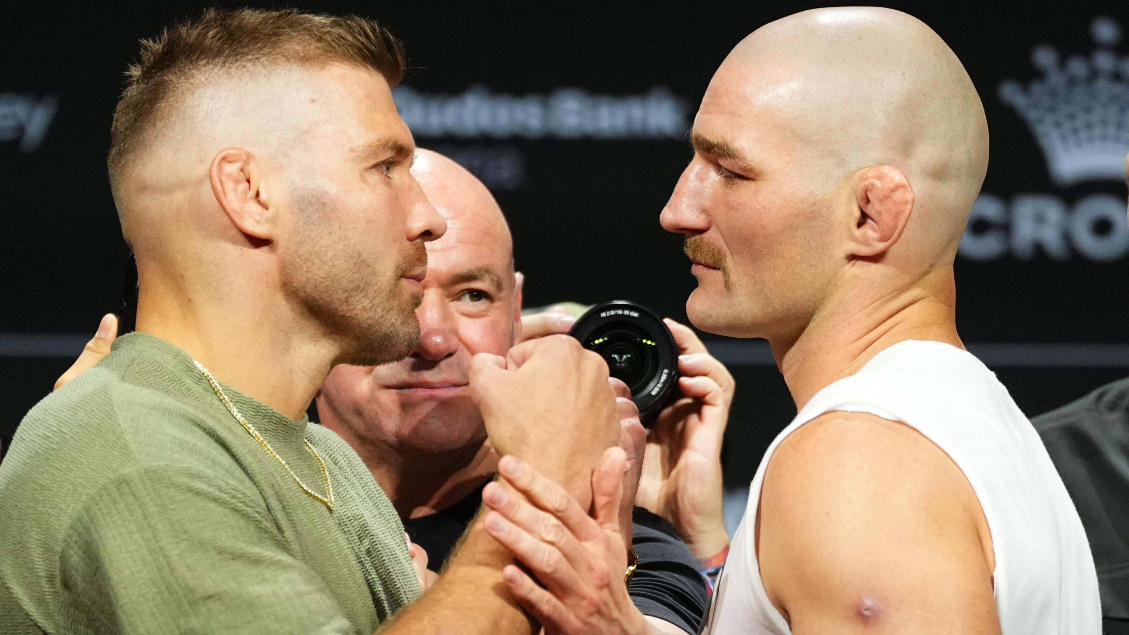 Dricus du Plessis, wearing a green T-shirt and gold chain, has his right fist held back by Dana White while the South African stands in front of Sean Strickland, who wears a white vest