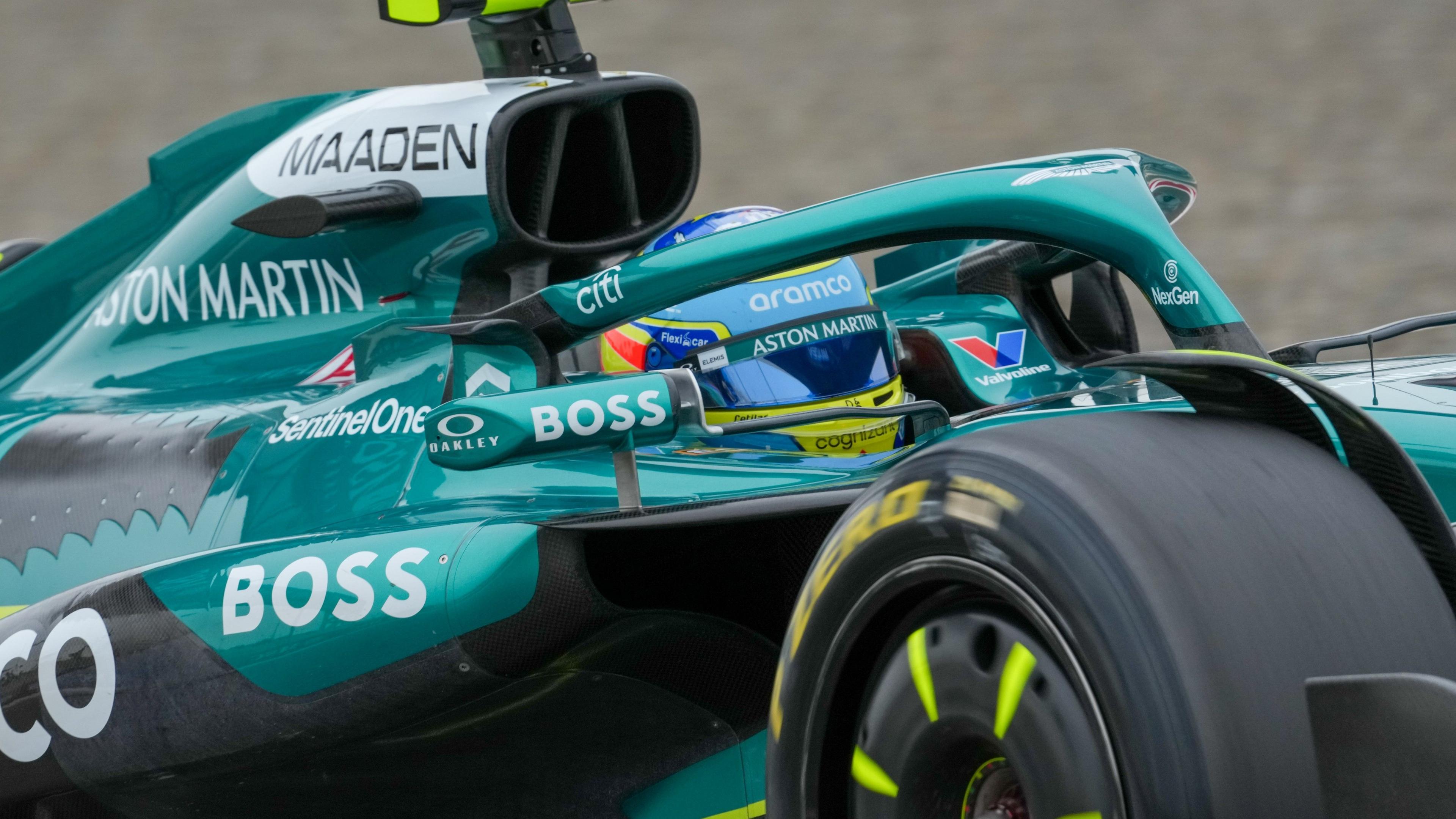 Close up of an Aston Martin Aramco F1 car with green livery and advertising, protective bars and within it, the helmet of a driver