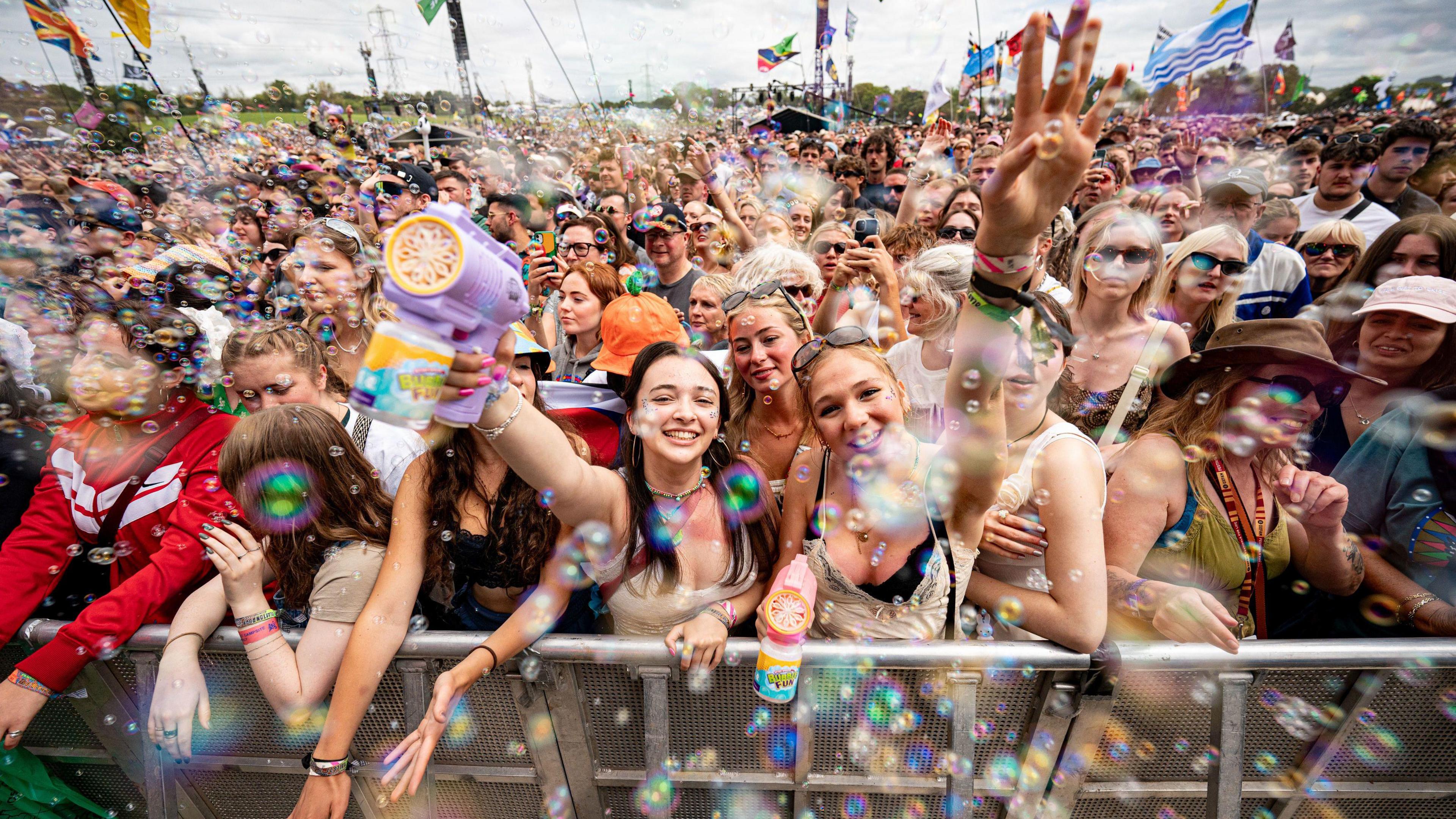 Music fans in a large crowd blow bubbles by the Pyramid stage