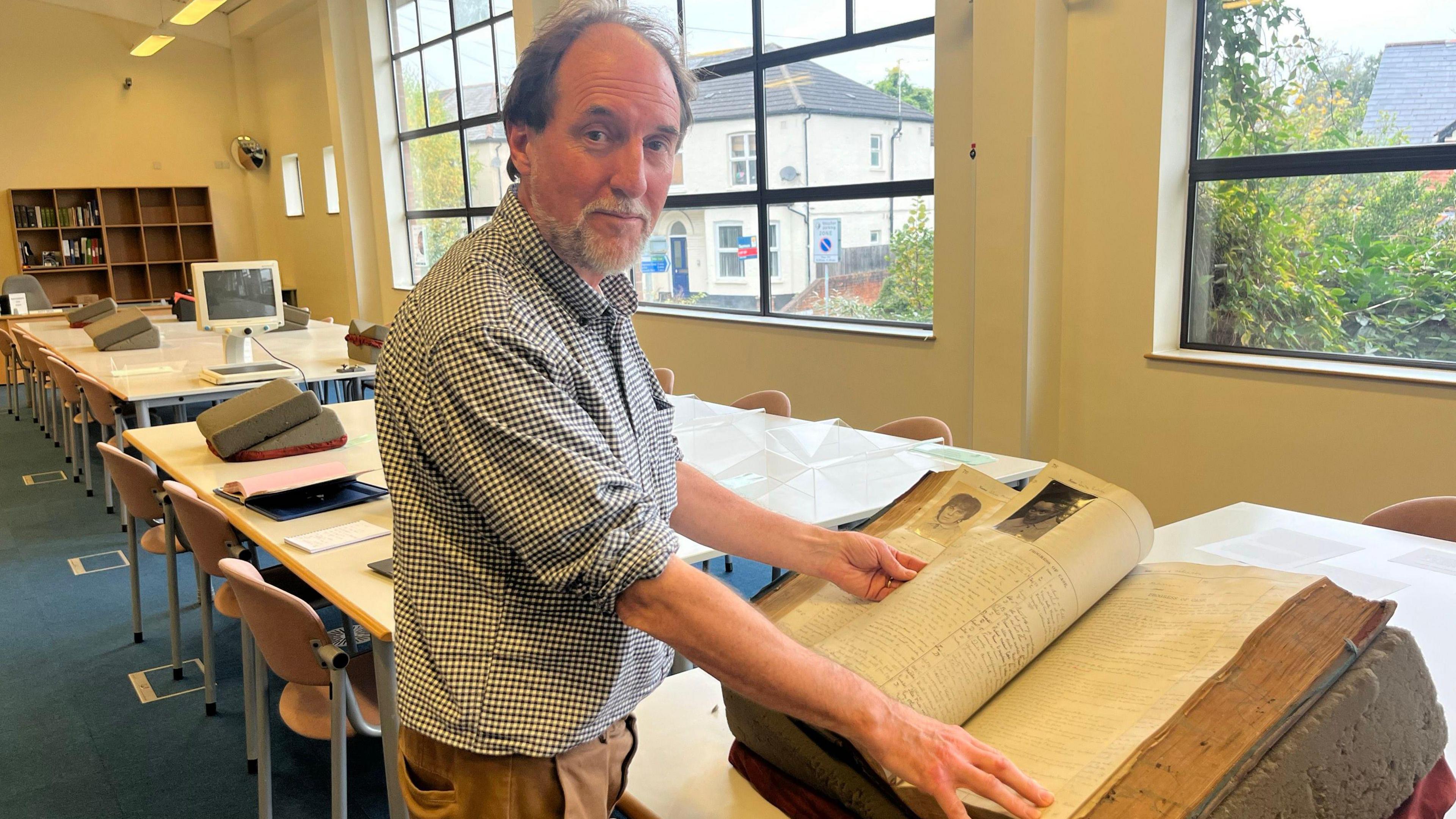 A historian wearing a check shirt looks at a record book filled with notes ad photographs of patients.