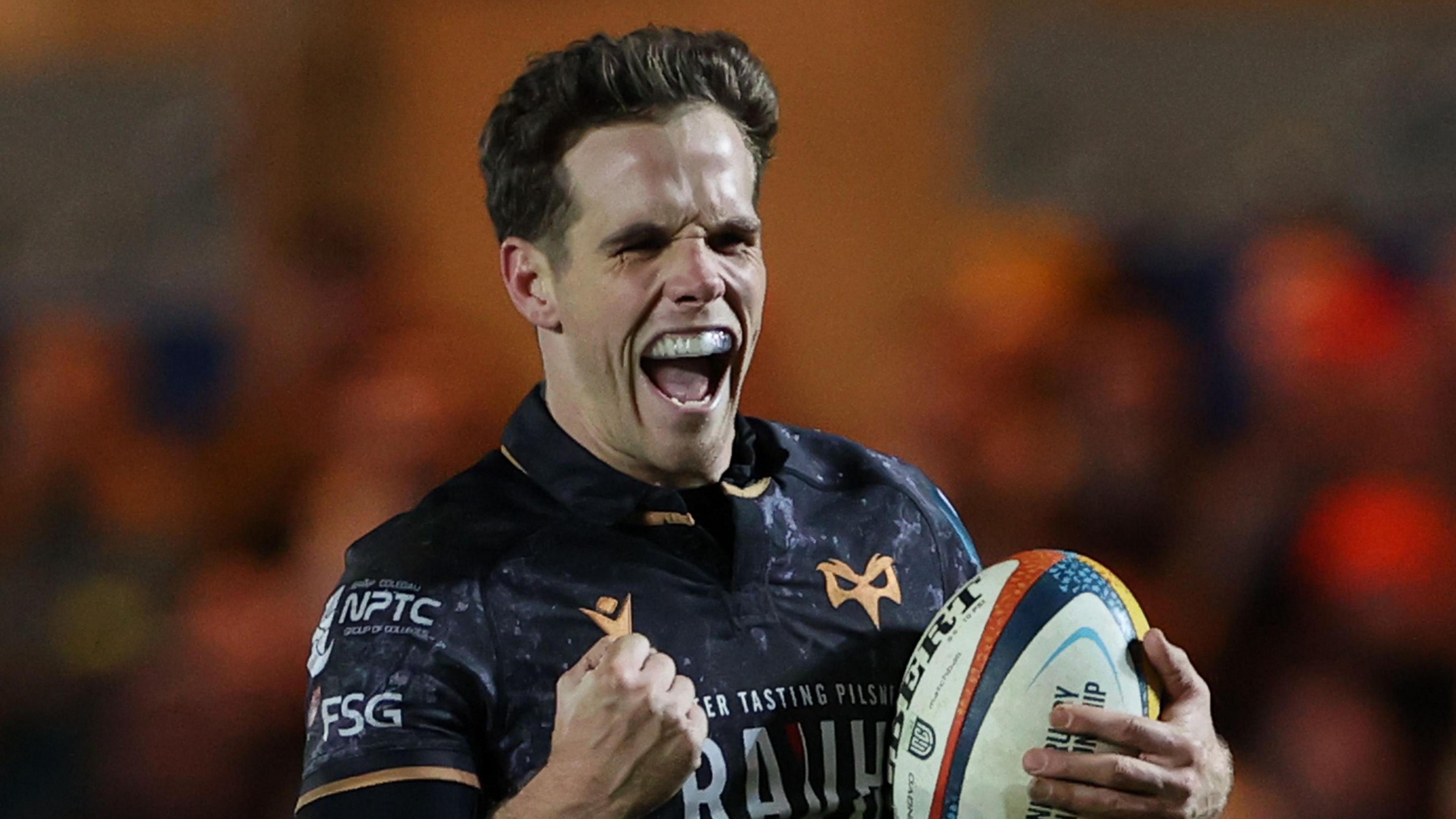 Kieran Hardy with ball in left hand grins and makes a first with his right hand as he runs in to score a try