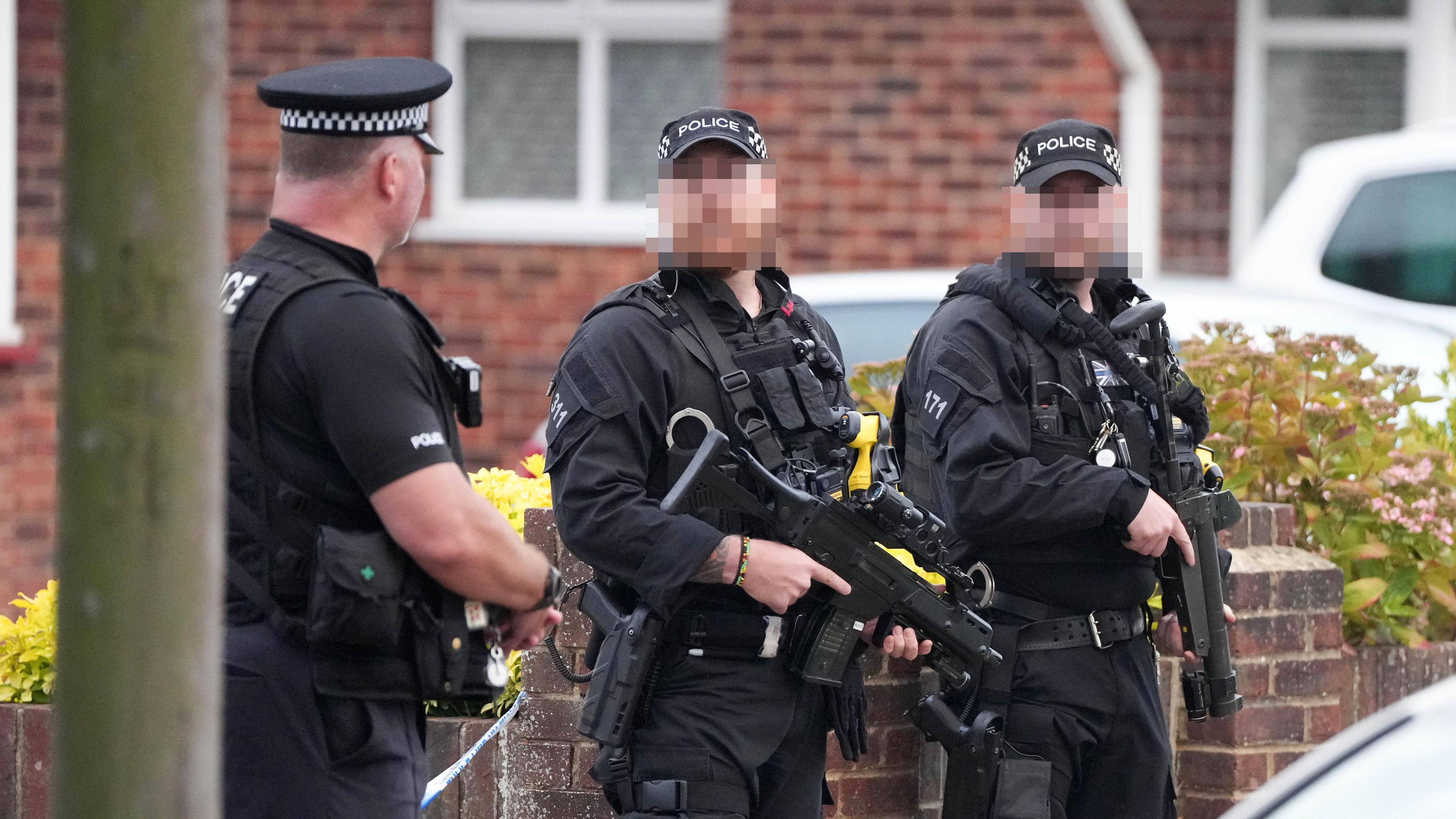 Three armed police at the scene of an incident in Lindum Road, Worthing. Two of the officers' faces are blurred out. All three are wearing black uniform and police caps. Two guns are visible in the image.