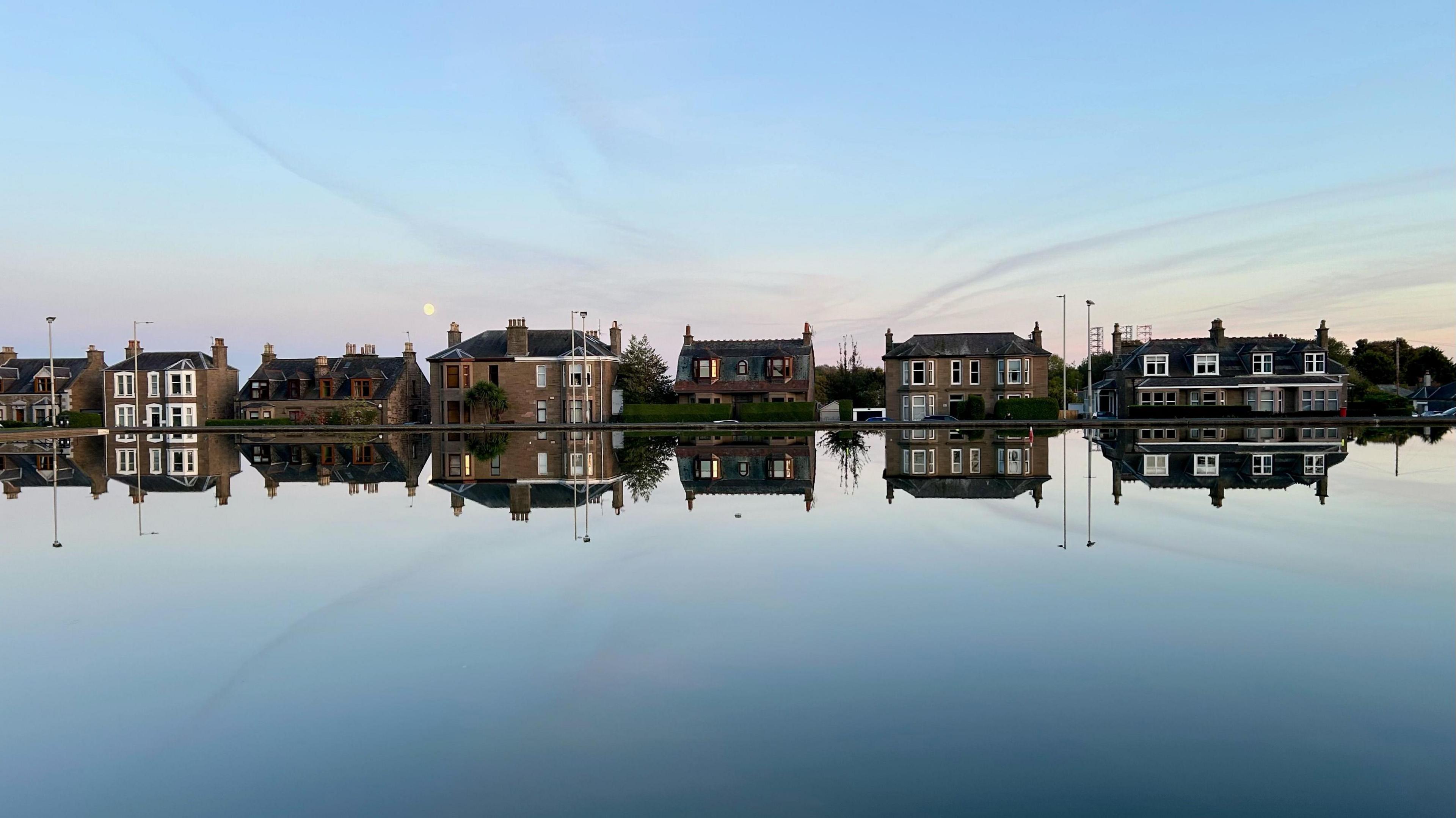 Houses perfectly mirrored on the water because it is so still.