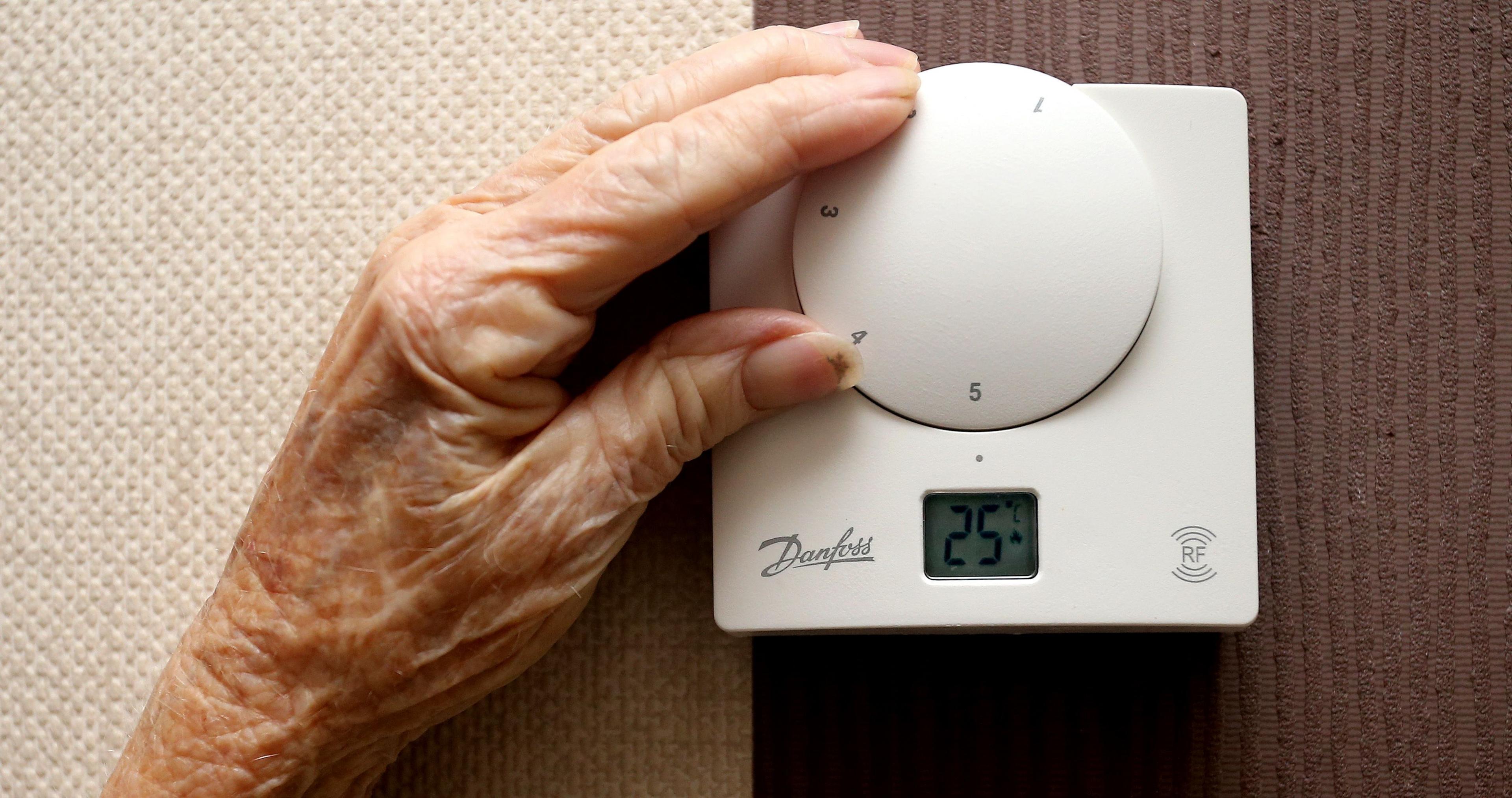 A wrinkled hand adjusts a thermostat.
