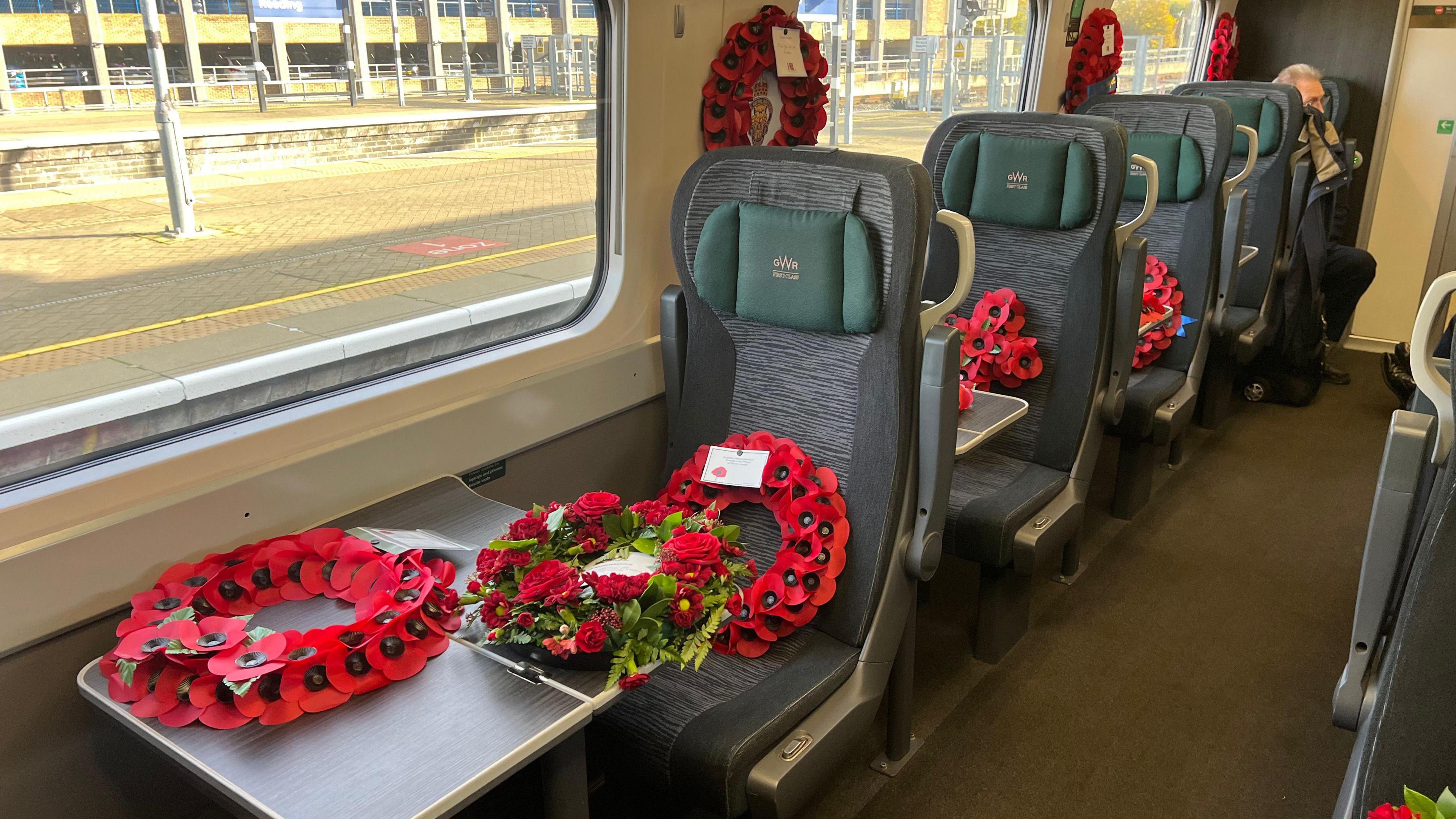 Rows of seats in the first class section of a Great Western Railway train. There are poppy wreaths placed on the tables and seats of the train.