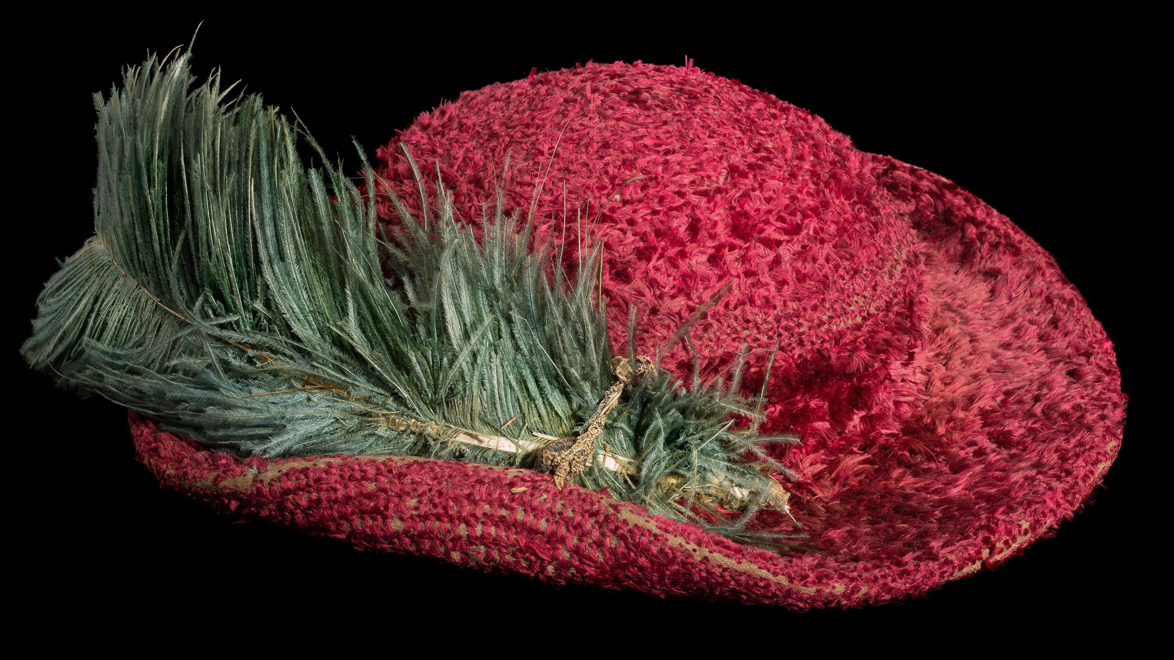 A bright red hat with a large green feather along the right hand side. 