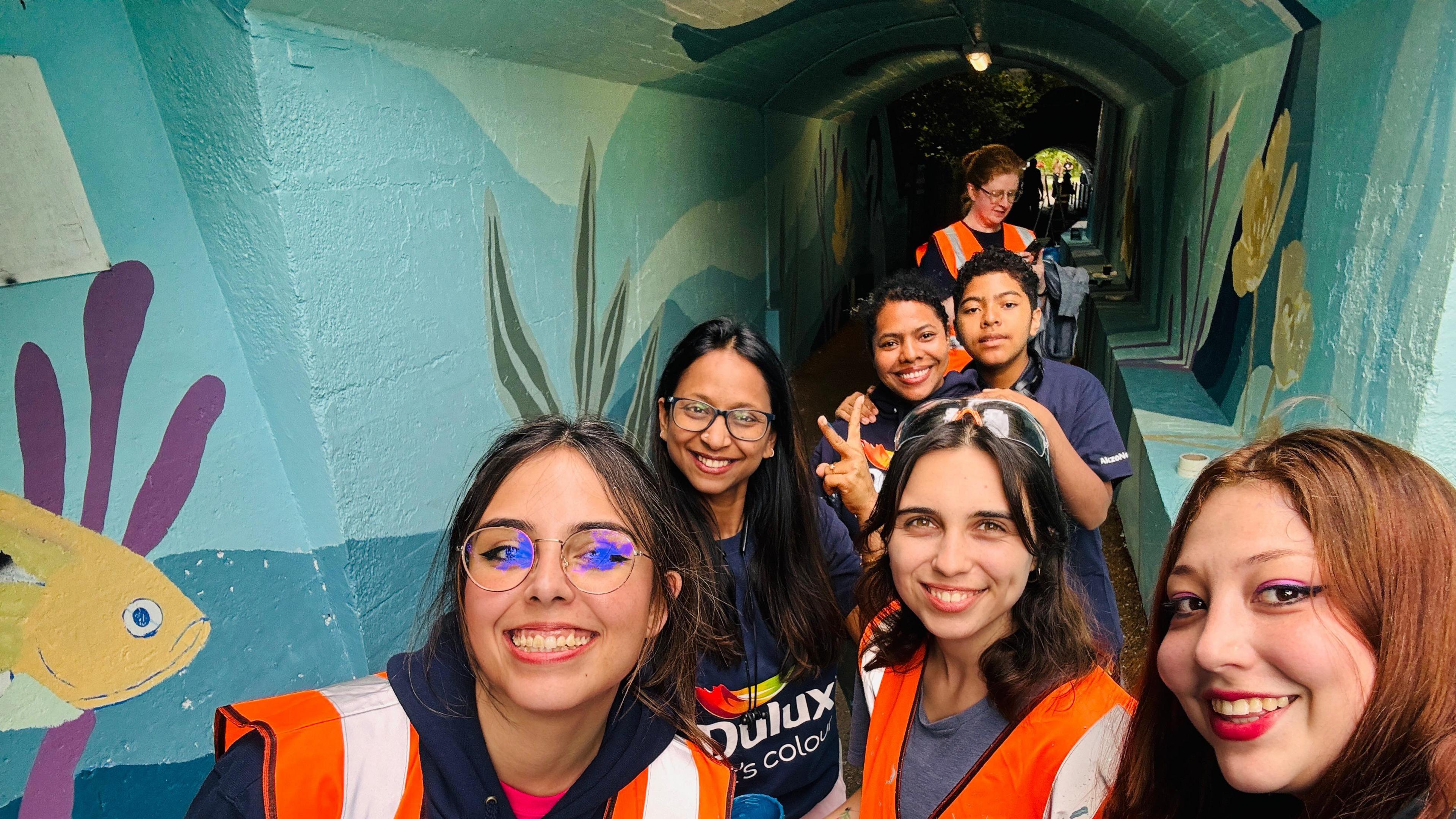 Volunteers smiling in a tunnel painted with an under-the-sea theme.