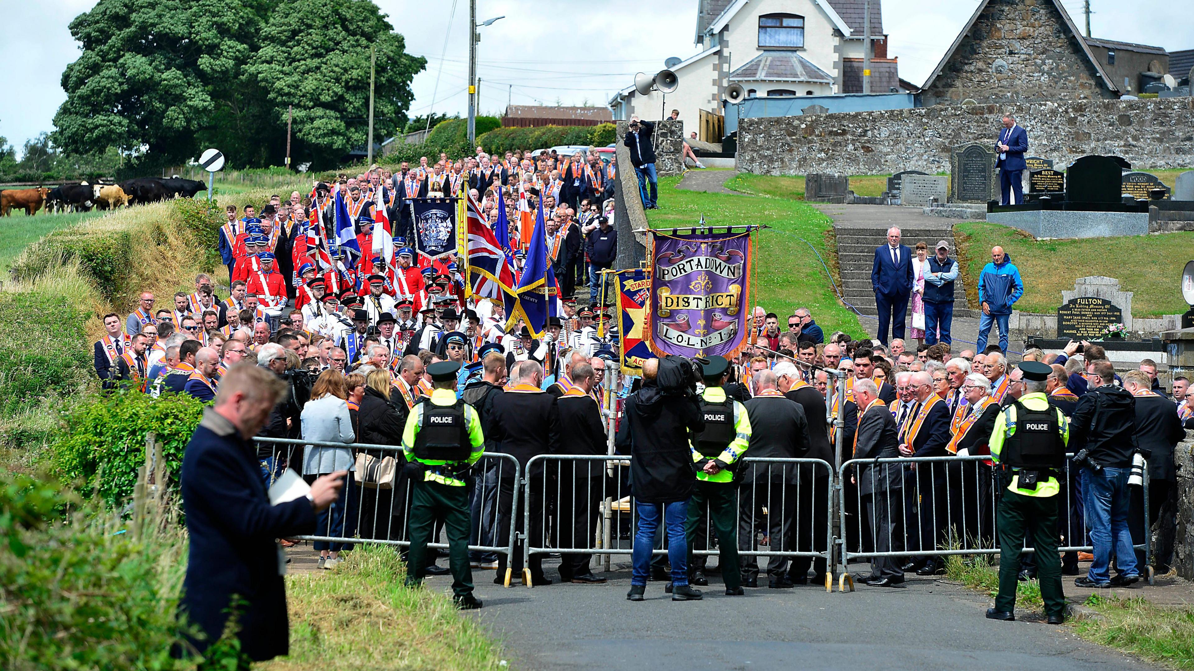 A large procession of Orange Order members being blocked by police from walking down a road. 