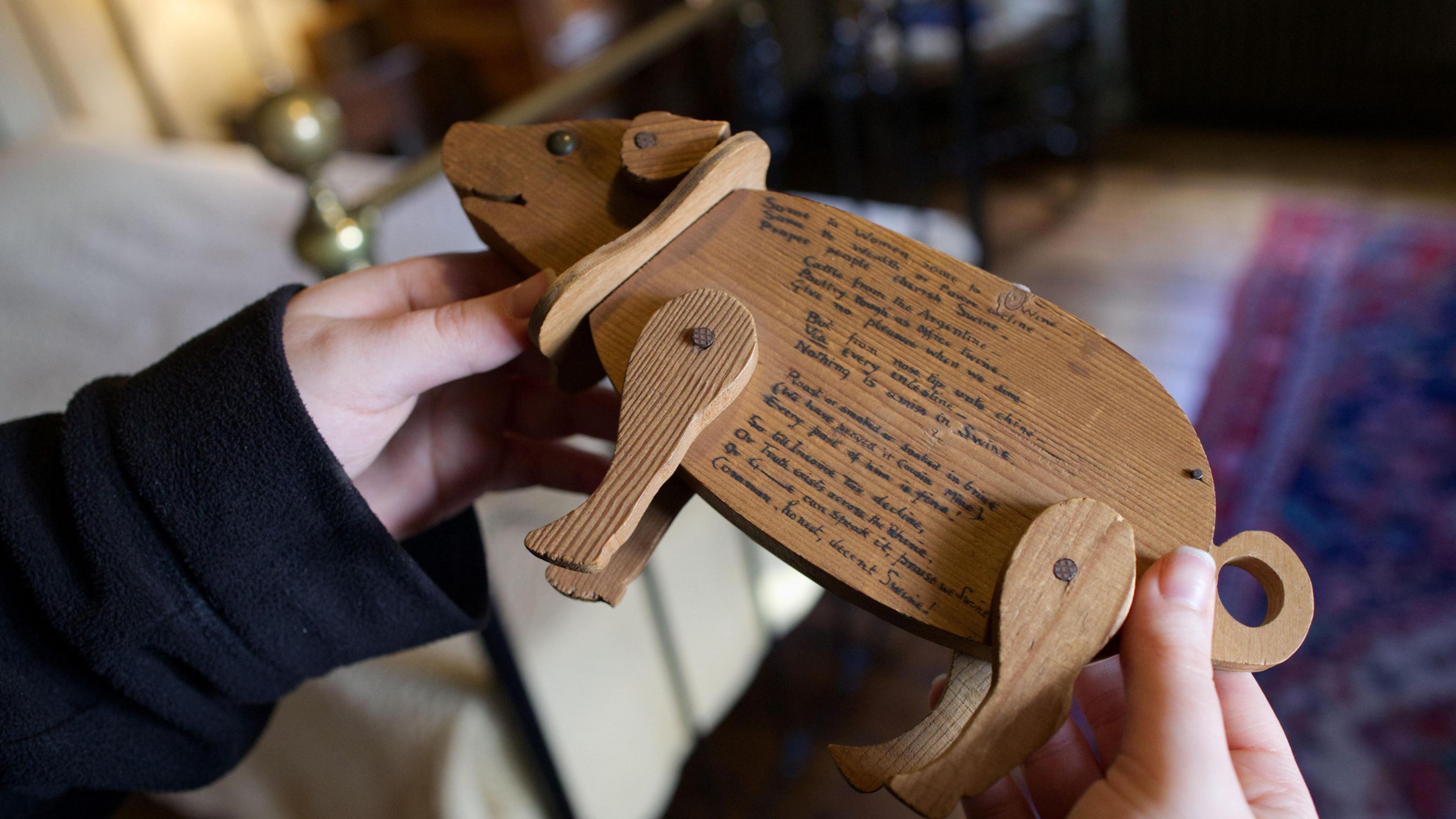 Two hands holding a wooden pig. The pig has writing on it, it is illegible. 