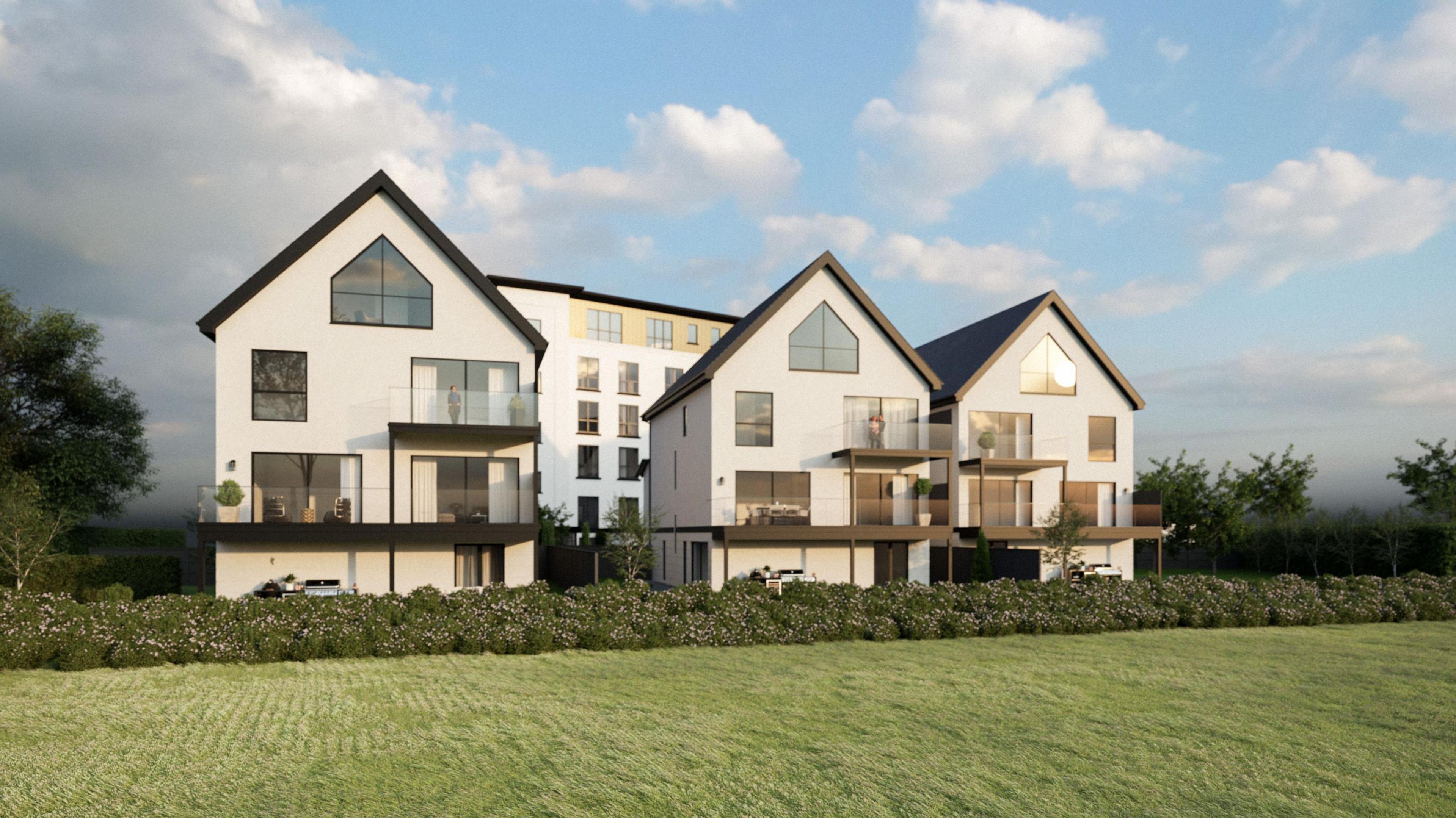 Three modern detached houses with balconies. The houses are white with black window frames and fascias, and a row of hedges and green field sits in front