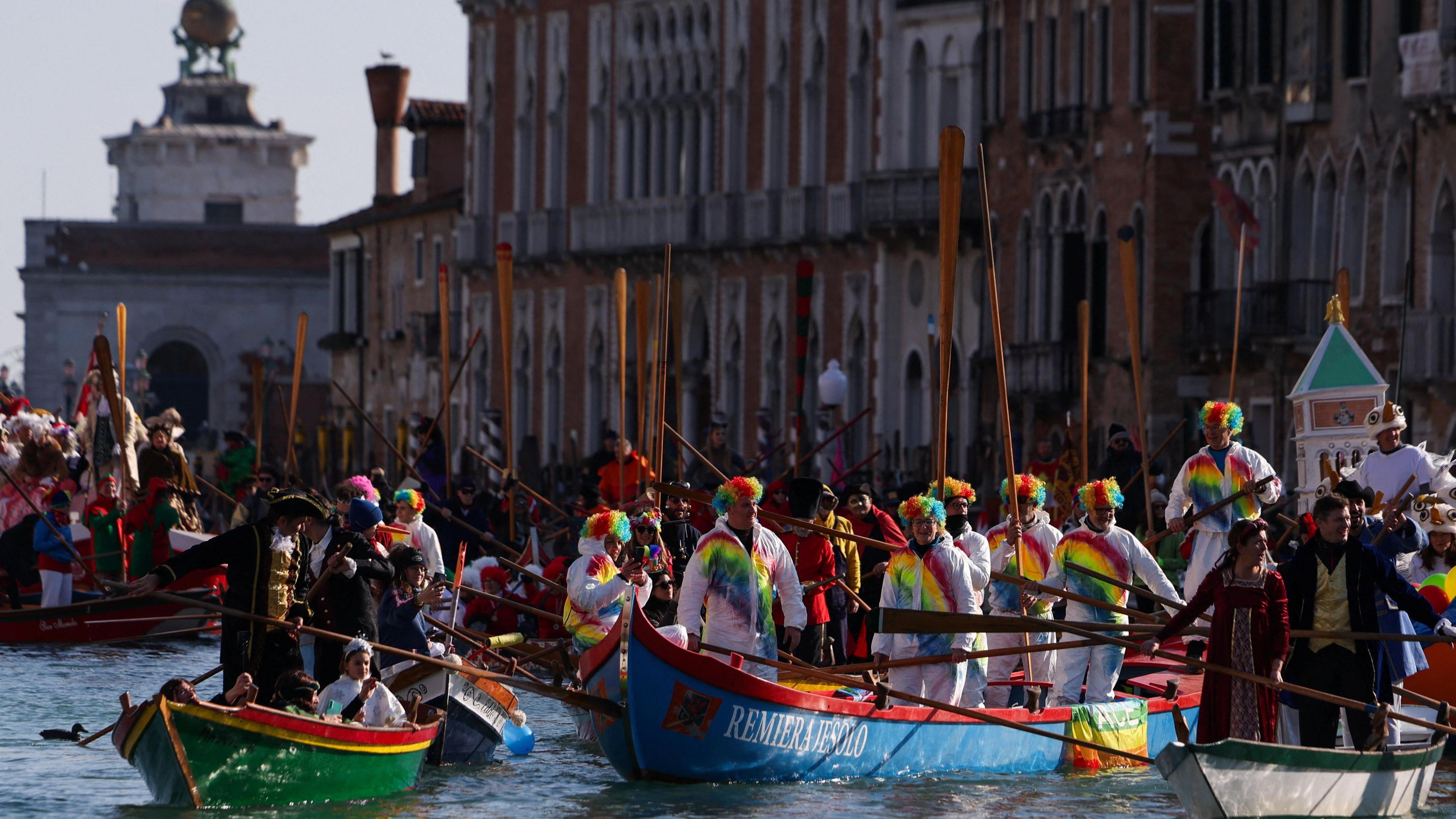 People dressed in rainbow colours are seen getting into boats.