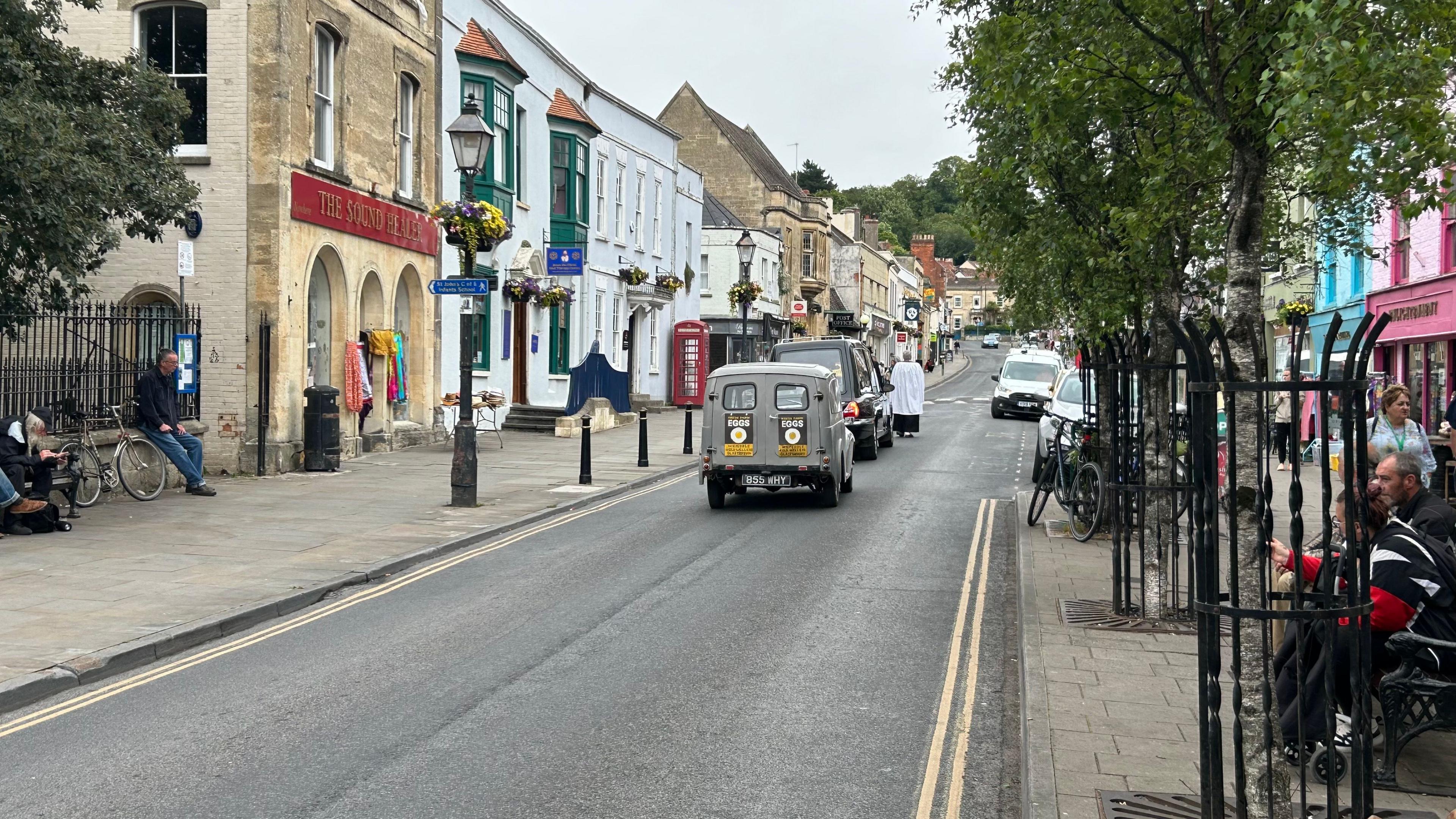 Wilf's Morris Minor van being driven up the high street