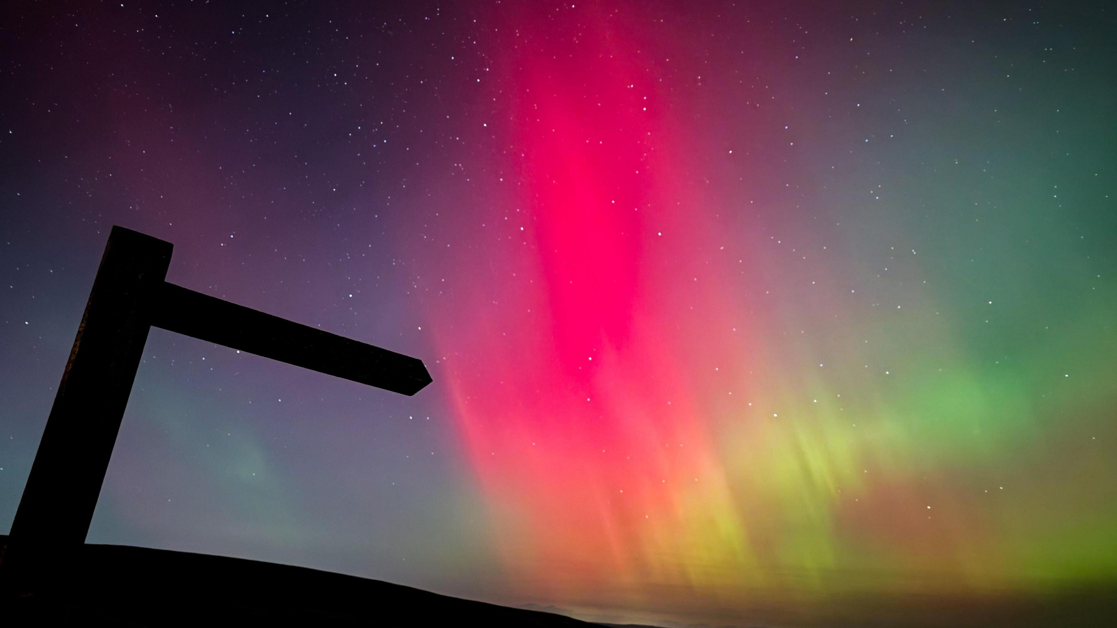 Pink, green and purple sky with a shadowed signpost in the foreground. 