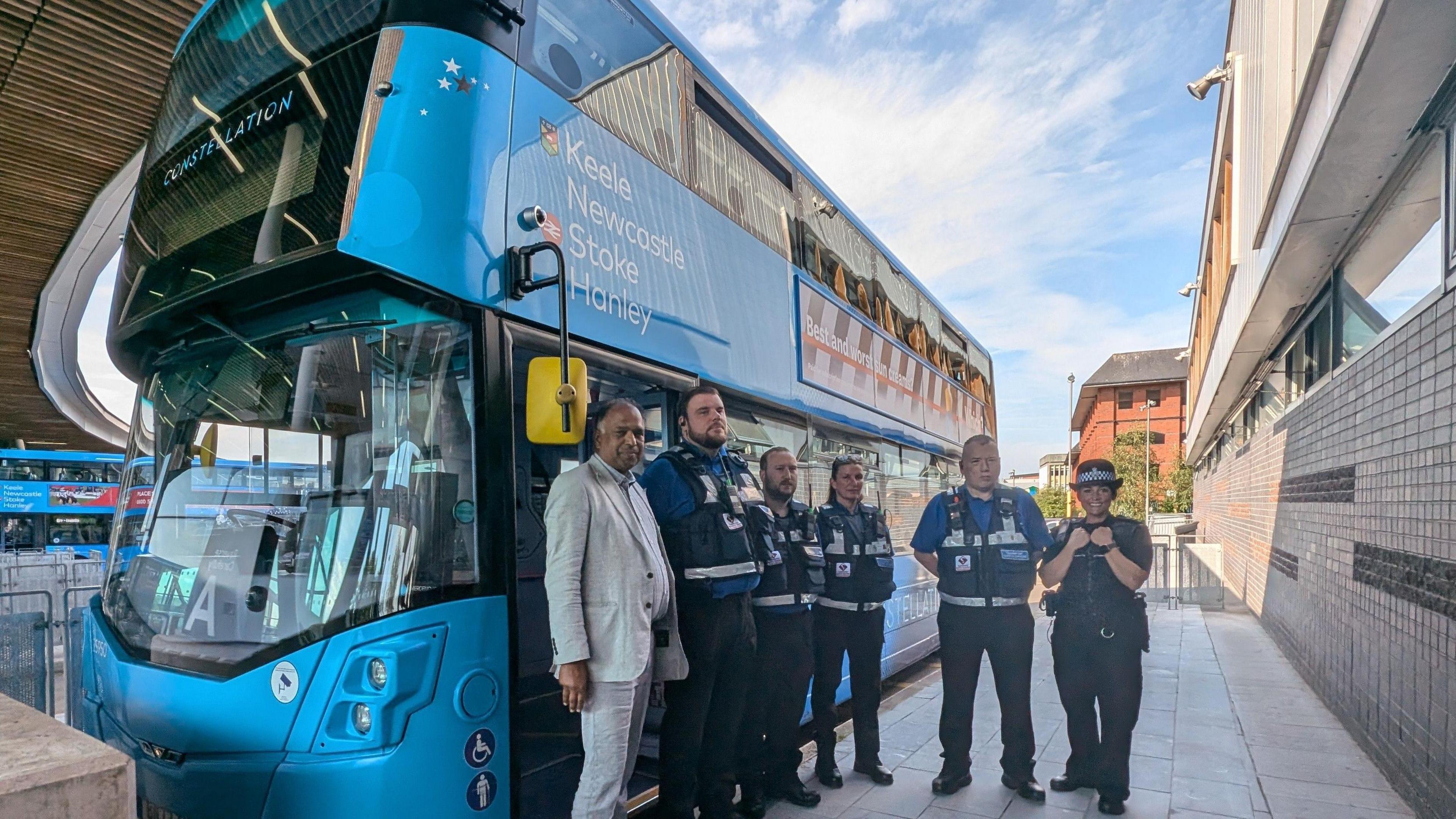 Four transport officers, deputy council leader Amjid Wazir and Chief Inspector Laura Davies from Staffordshire Police standing outside on a sunny day next to a blue bus