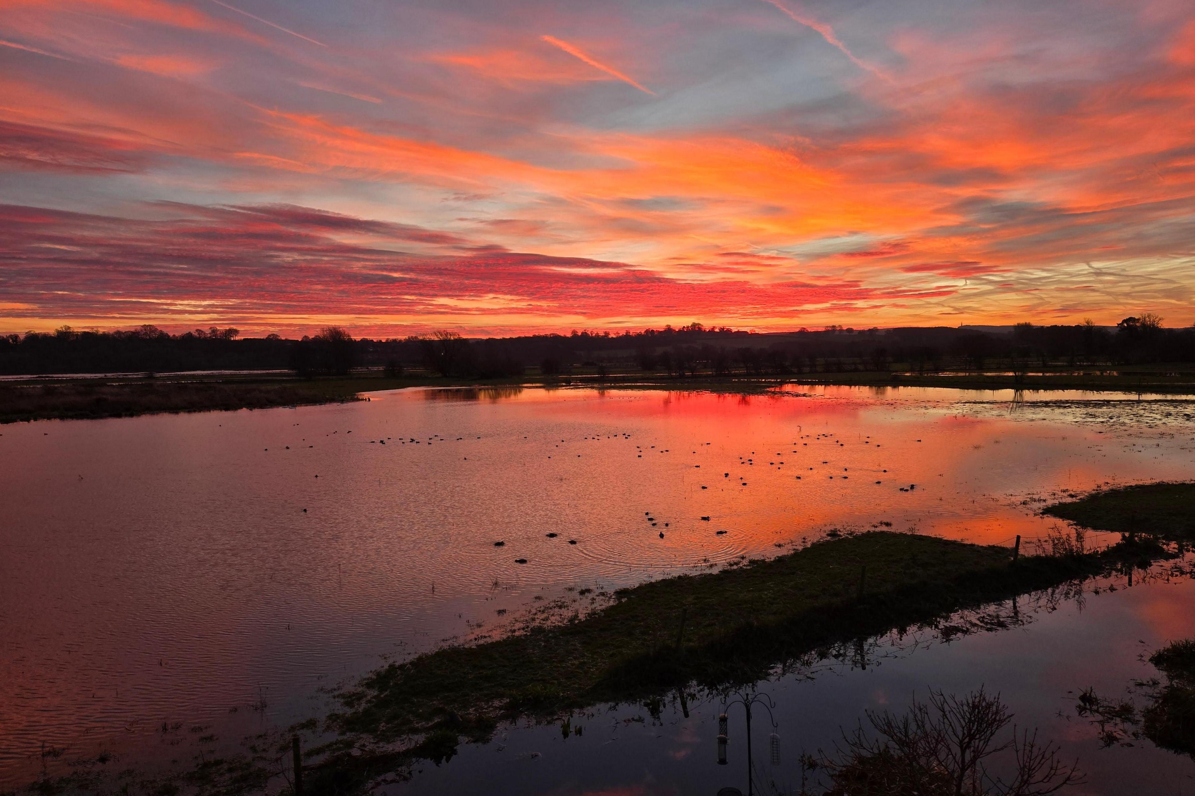 The sky extensively features red and orange. The sky's reflection is on the water, which makes up at least half of the image.