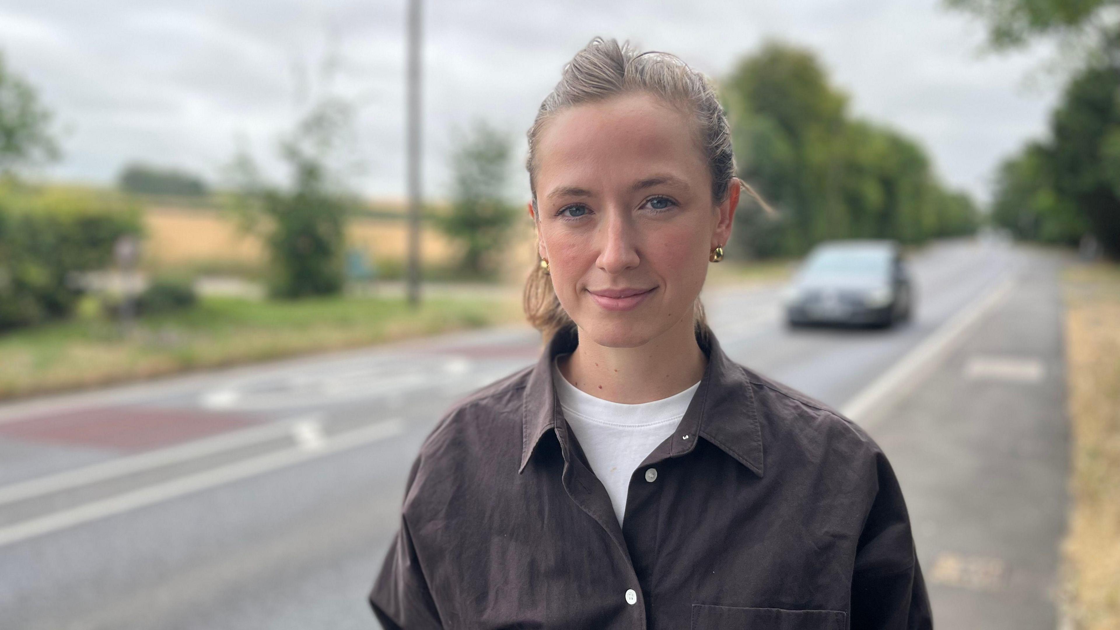 Head and shoulders image of Anna Ross. She has brunette hair tied up, is wearing a brown shirt over a white t-shirt